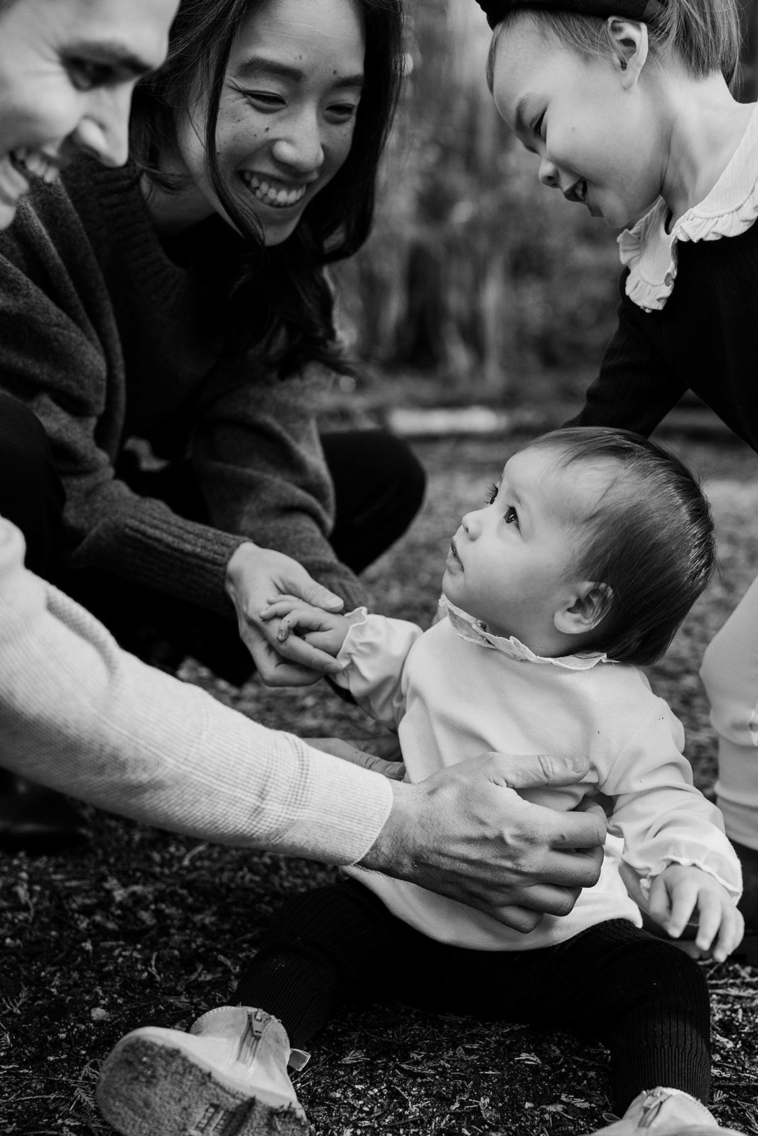 Black and white photo series showing playful interaction between baby and parent lying on ground.