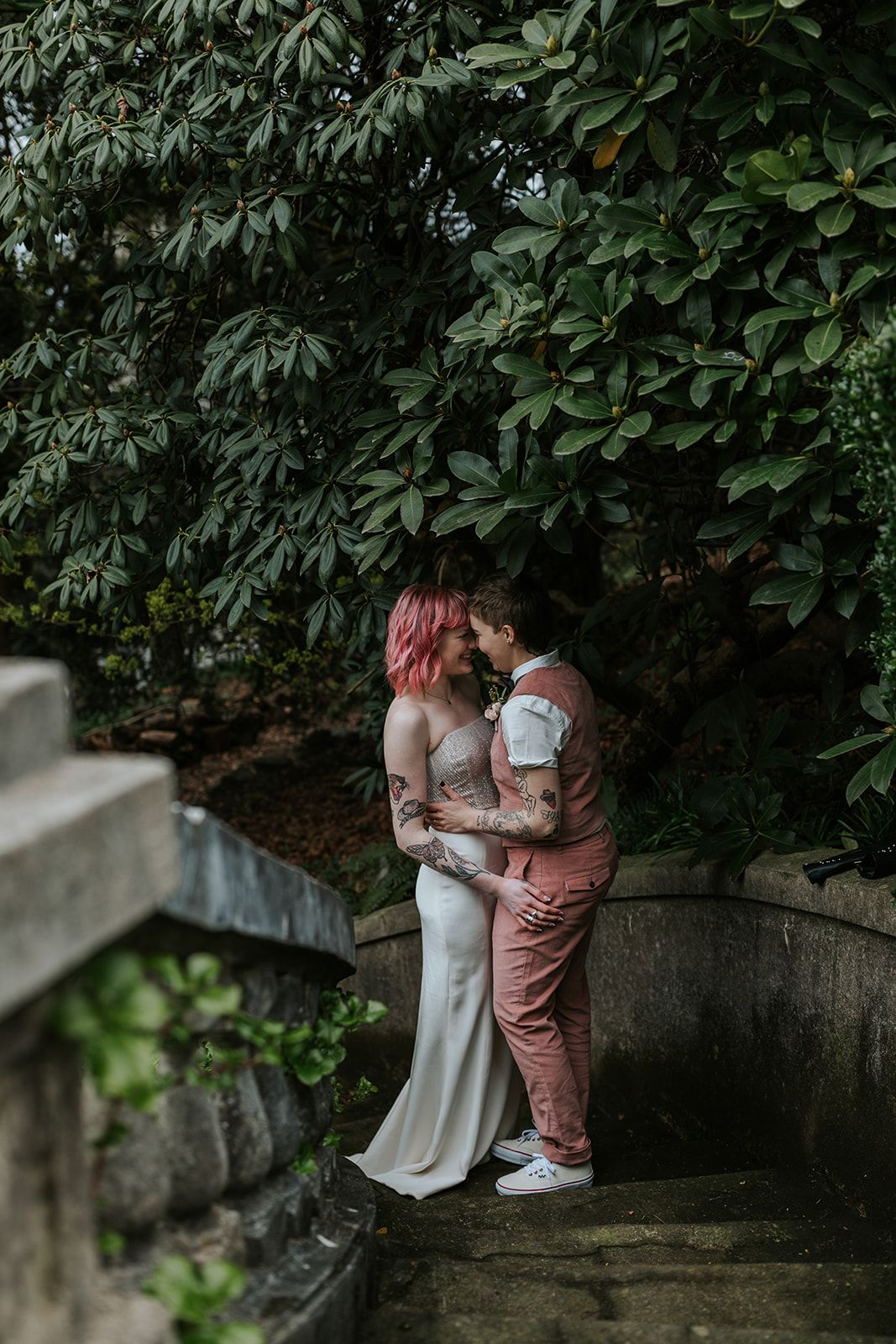 A romantic moment between newlyweds on stone steps surrounded by lush green foliage.