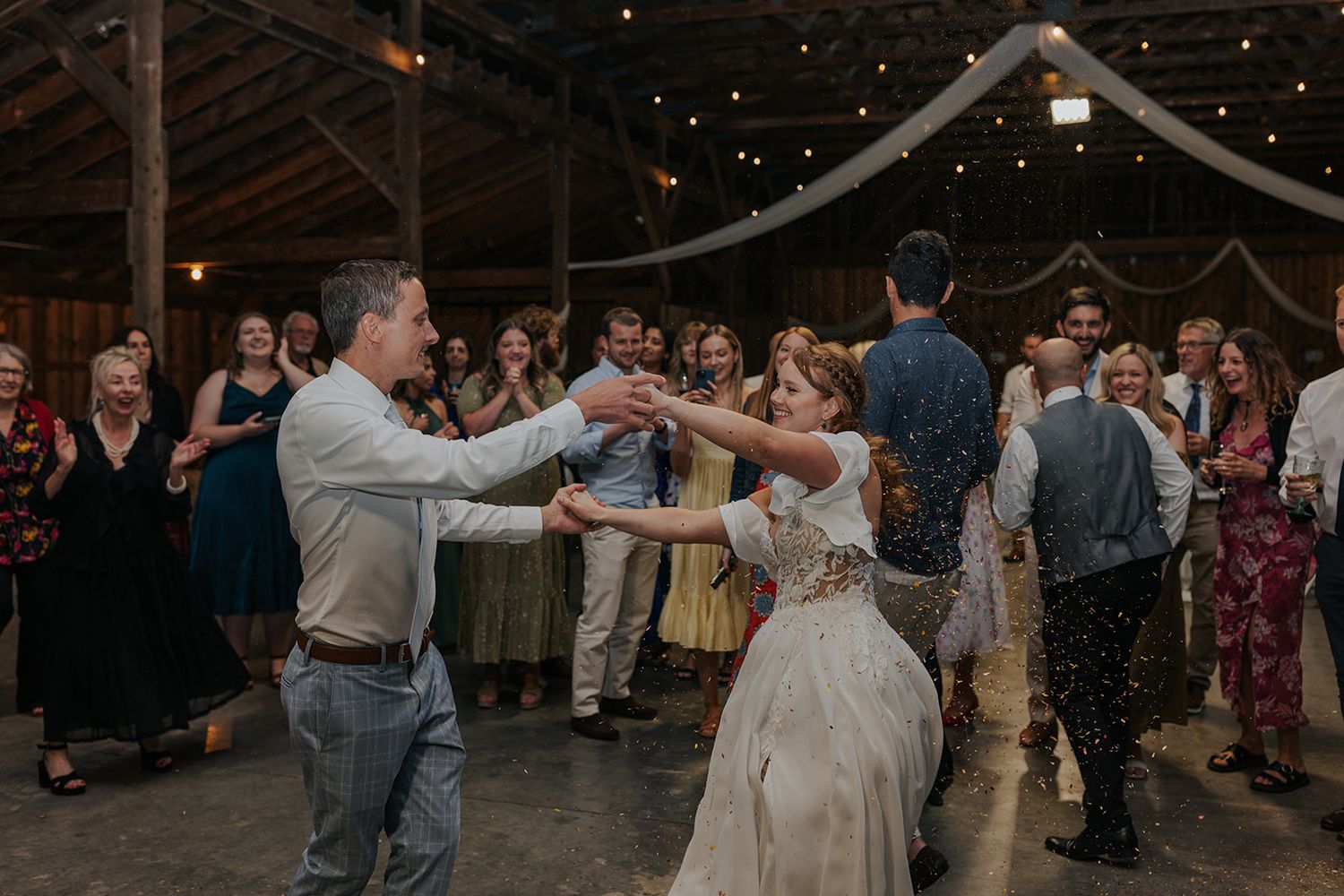 Wedding guests dancing together under twinkling lights in a rustic barn venue.