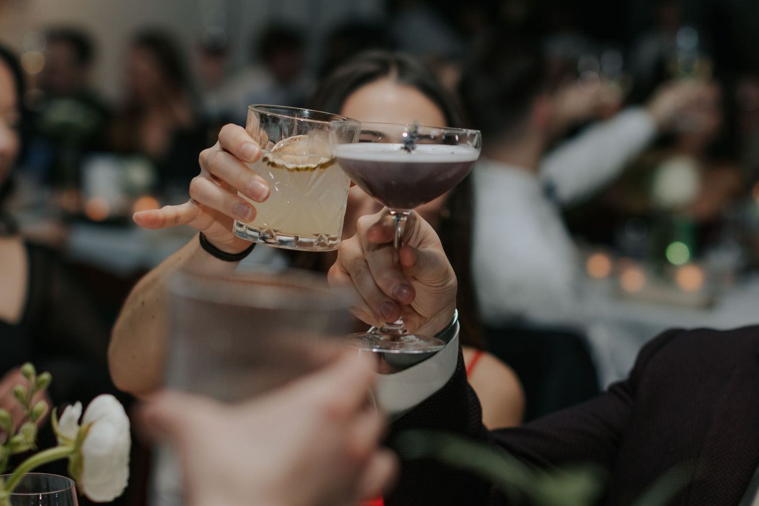 Guests raise cocktail glasses in celebration at a dimly lit reception.