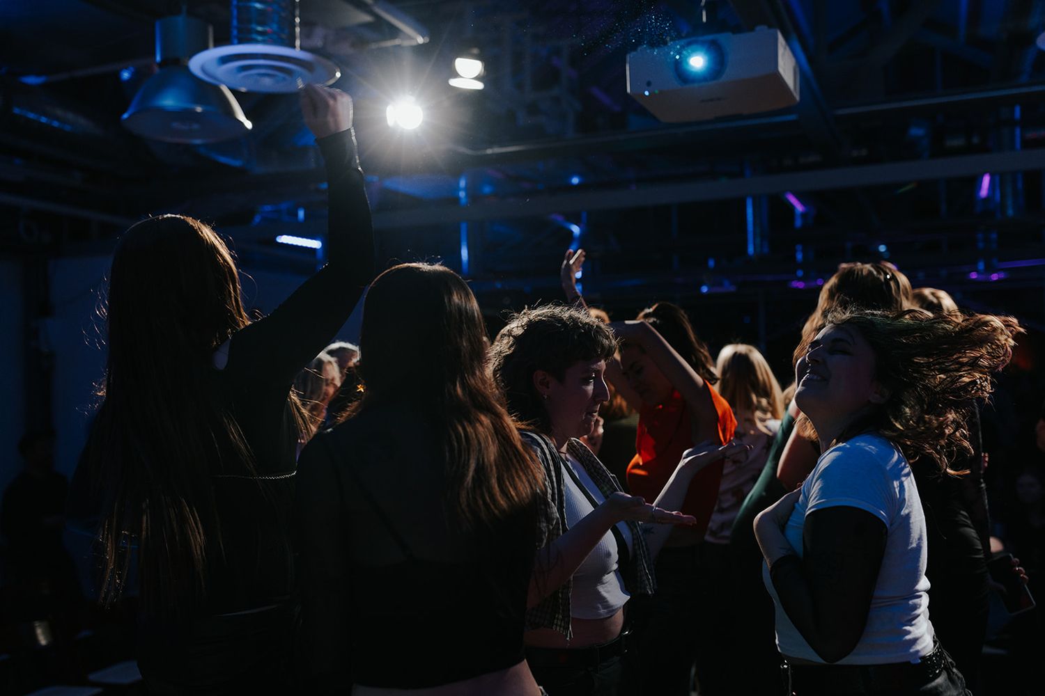 Concert crowd silhouettes with blue stage lighting and performers creating an energetic atmosphere at a live show.