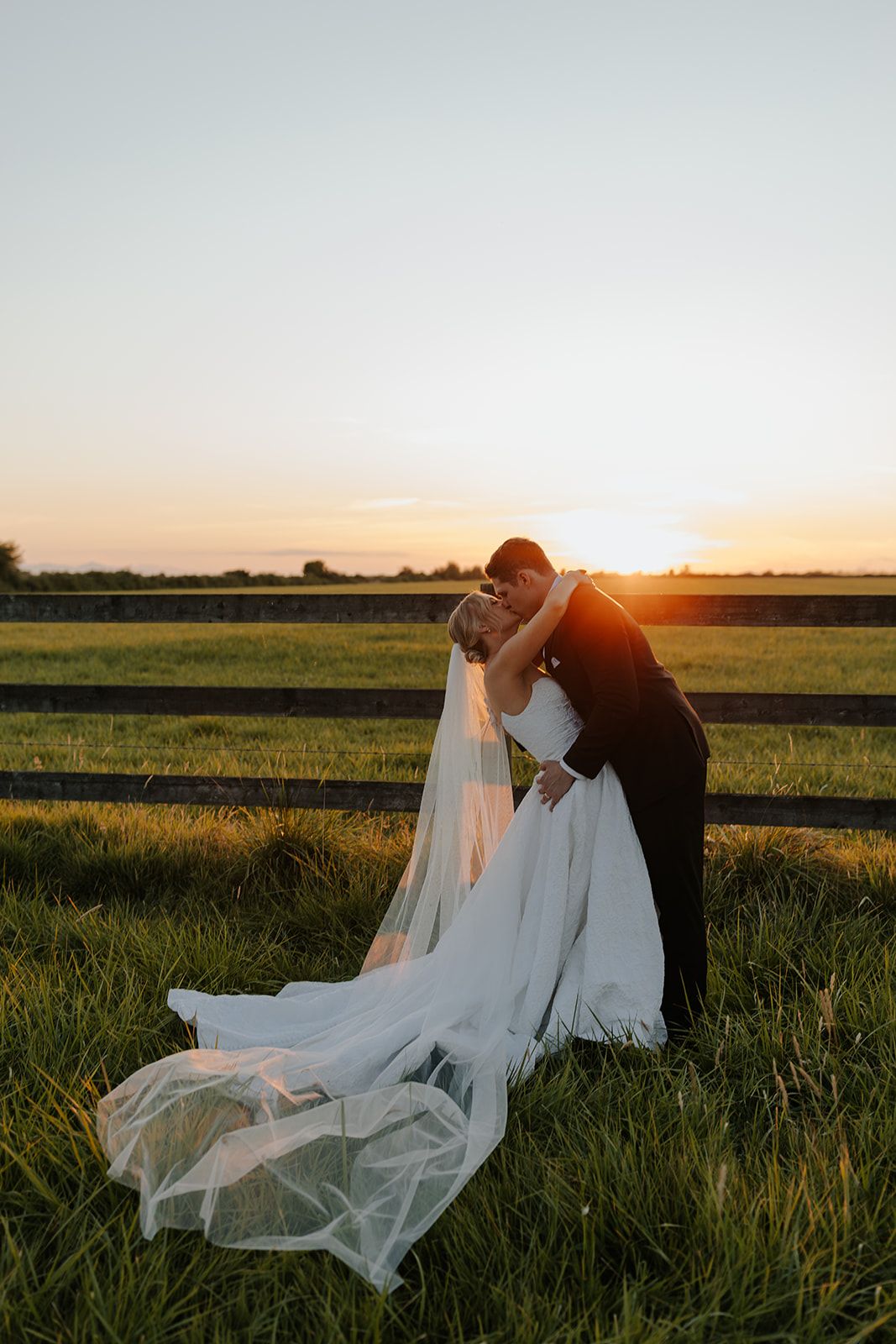 Romantic sunset wedding portrait in a grassy field with flowing veil.