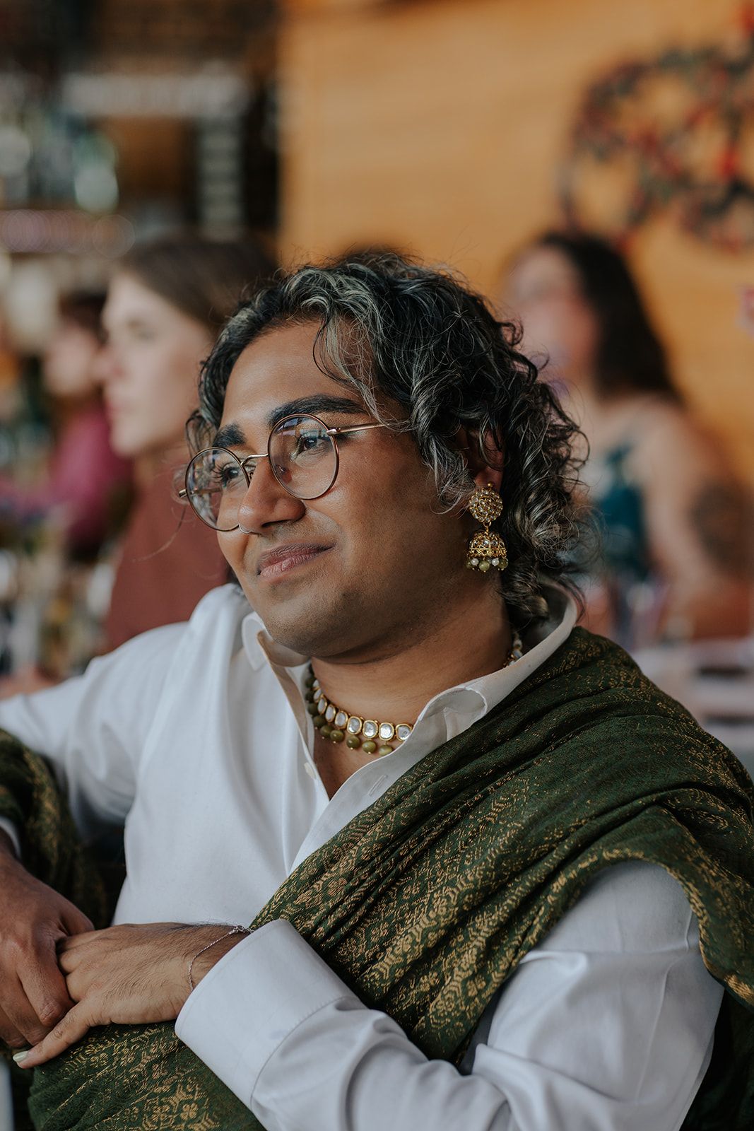 Guest wearing traditional sari and pearls smiles during wedding celebration.