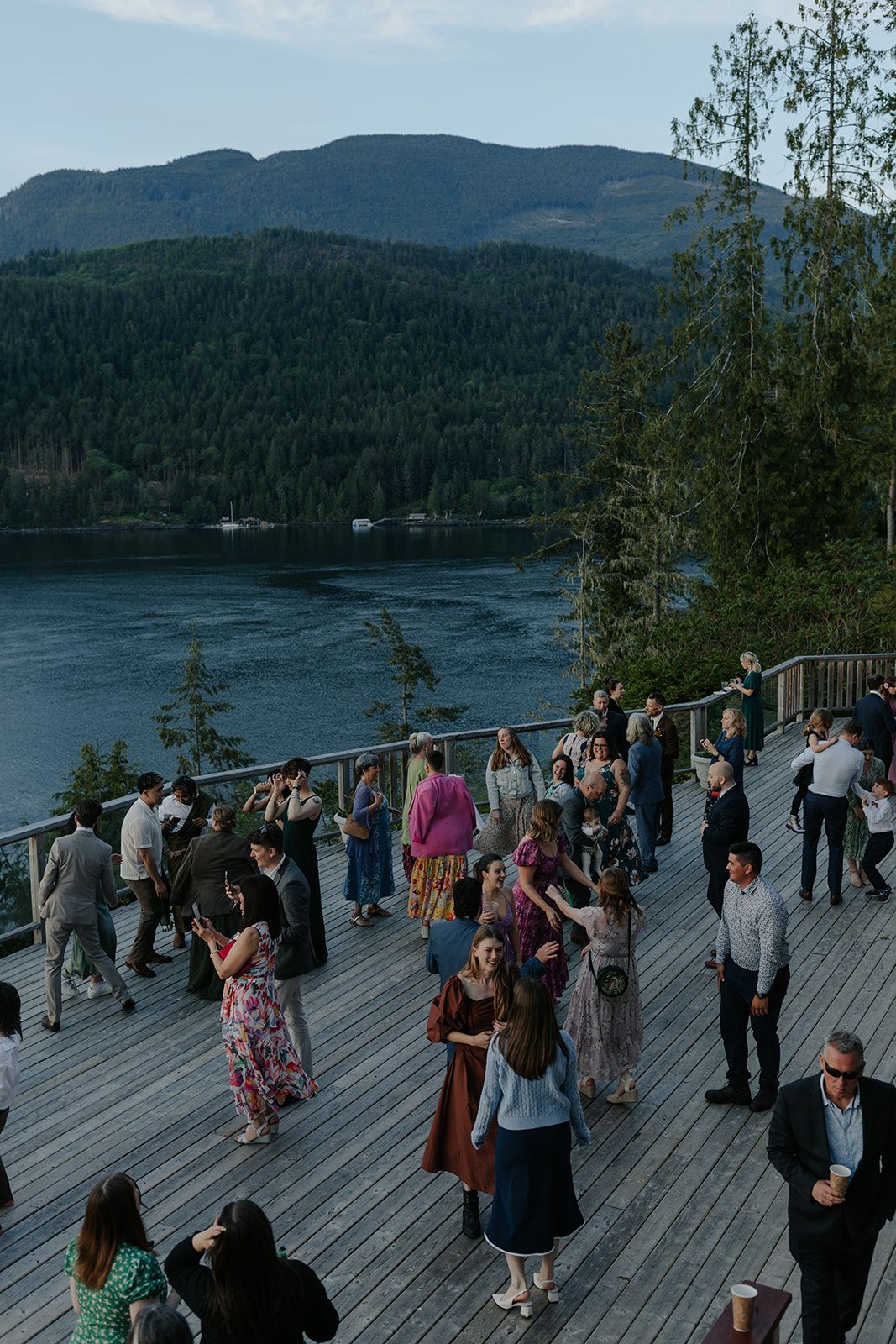 Wedding guests dance and celebrate on an outdoor deck with mountain and lake views.