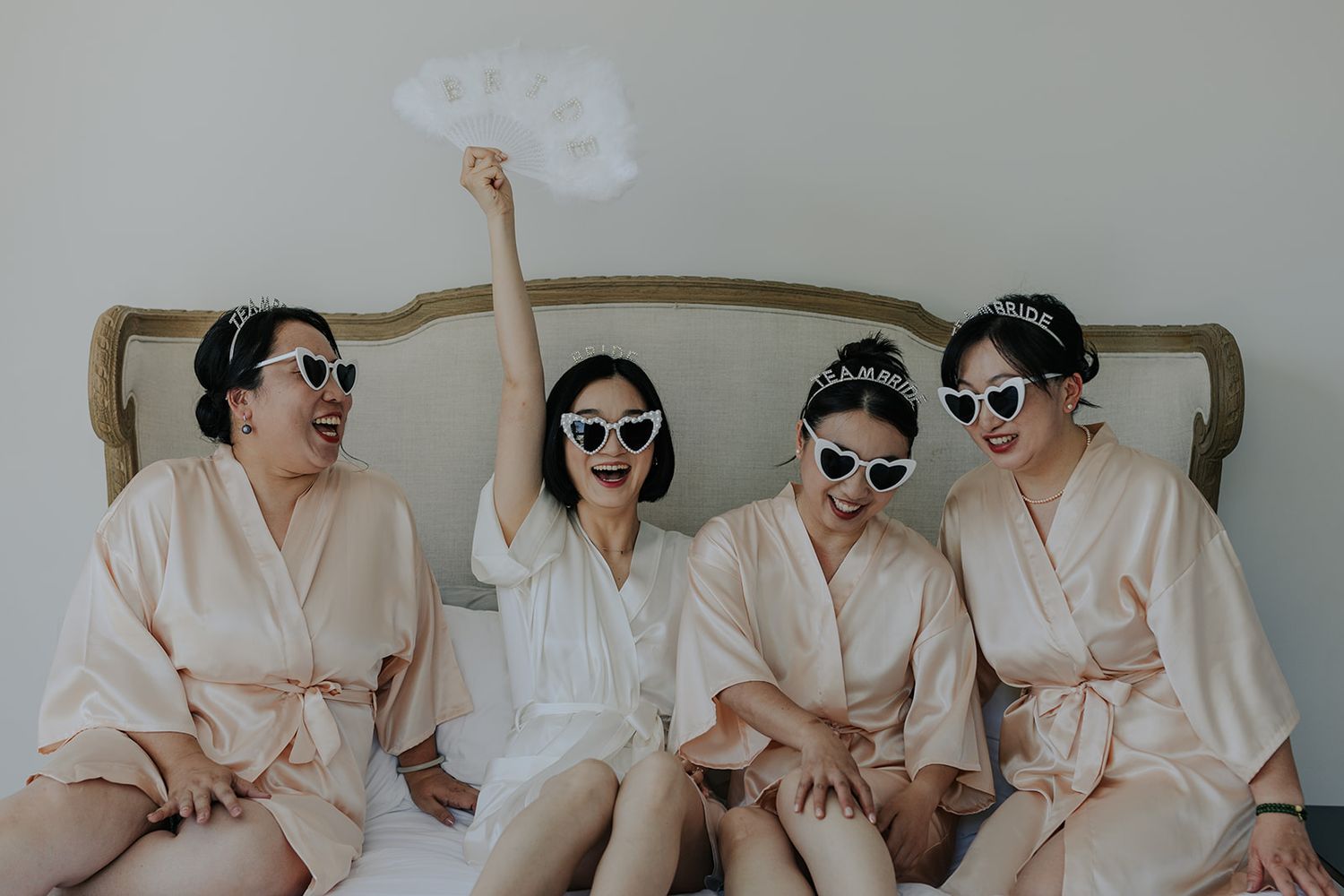 Bridesmaids in pink robes laugh together during pre-wedding preparations.