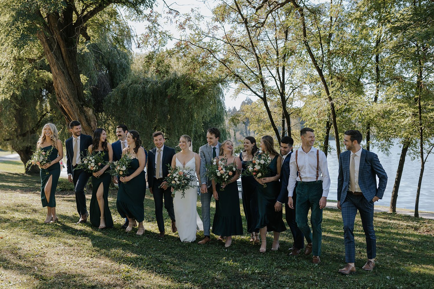 Wedding party poses together outdoors along a tree-lined path.