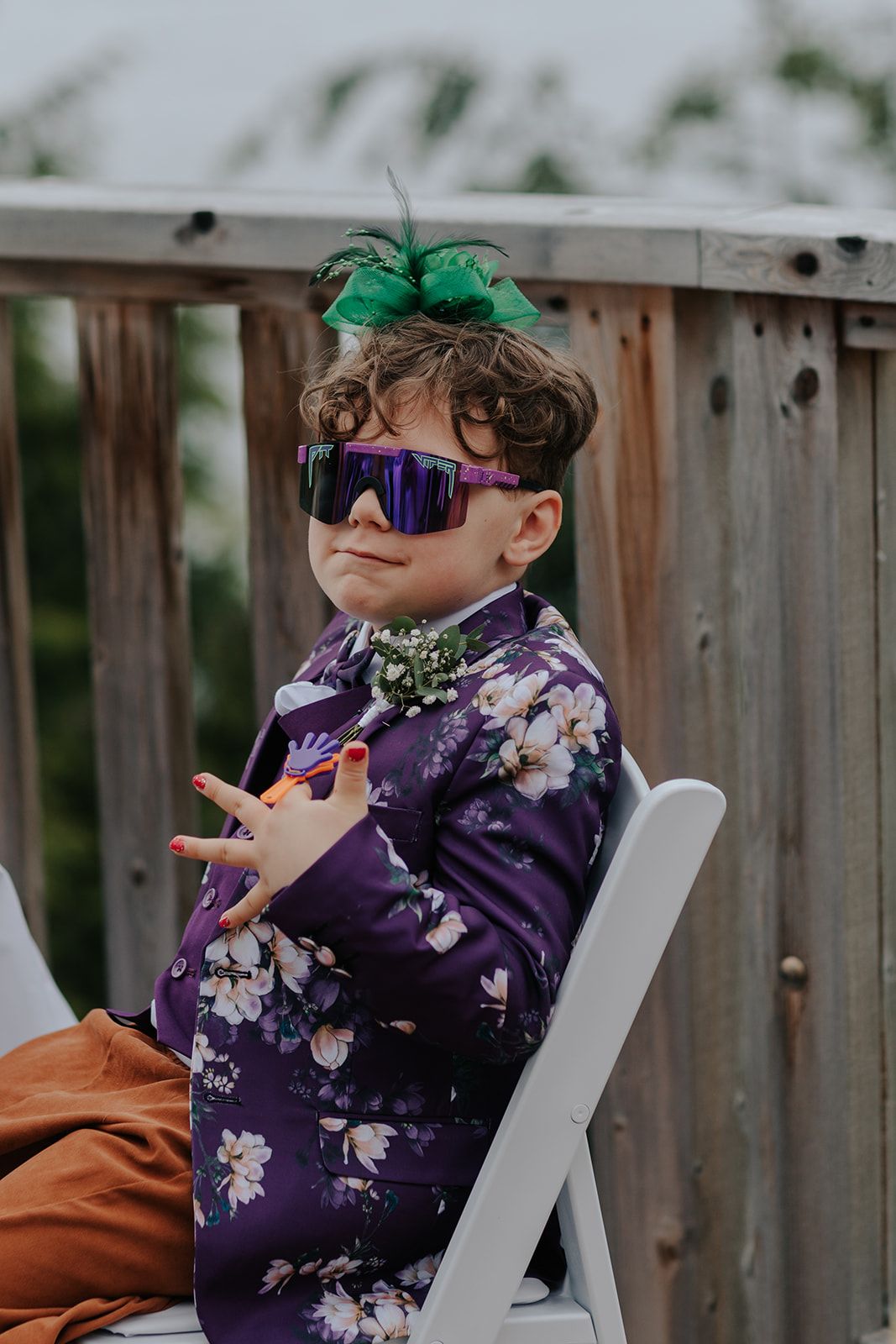 Young guest in purple floral attire and sunglasses sitting at outdoor wedding.