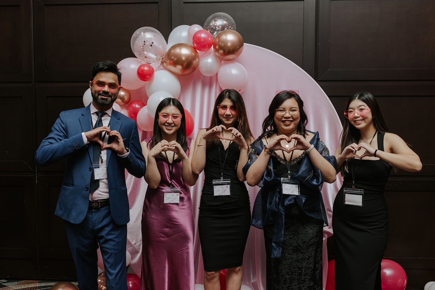 Group photo with pink and silver balloon decorations in a dark-themed venue.