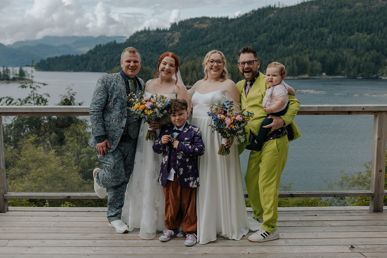Wedding guests pose together on scenic overlook with mountain and lake vista.