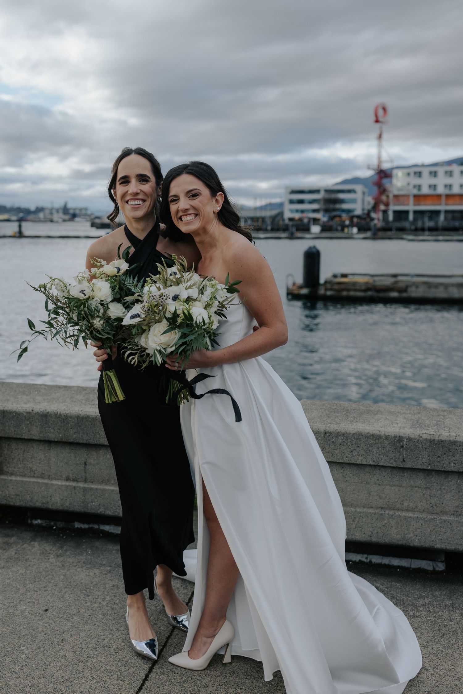Wedding party members posing with bouquets along a waterfront promenade.