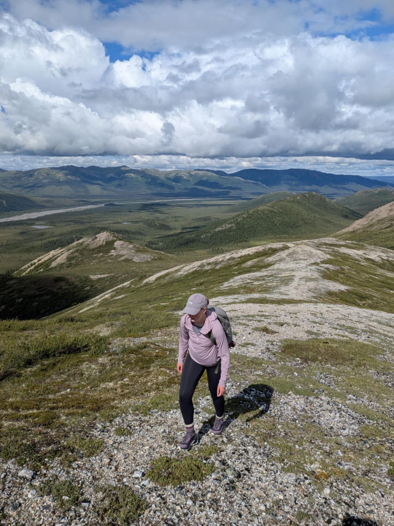 Hiker climbing rocky mountain terrain under dramatic cloudy sky.