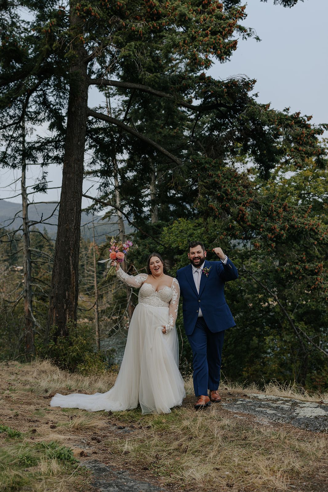 Wedding couple celebrates on rocky cliff overlooking scenic mountain landscape.