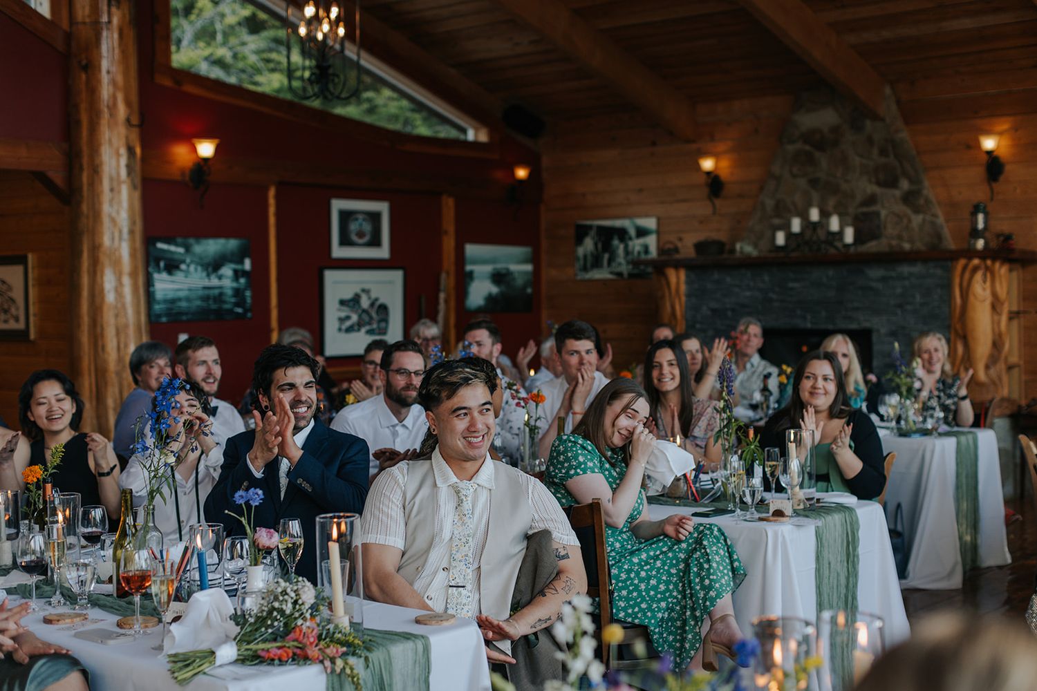 Wedding guests seated in a rustic wood-paneled reception hall with lake views.