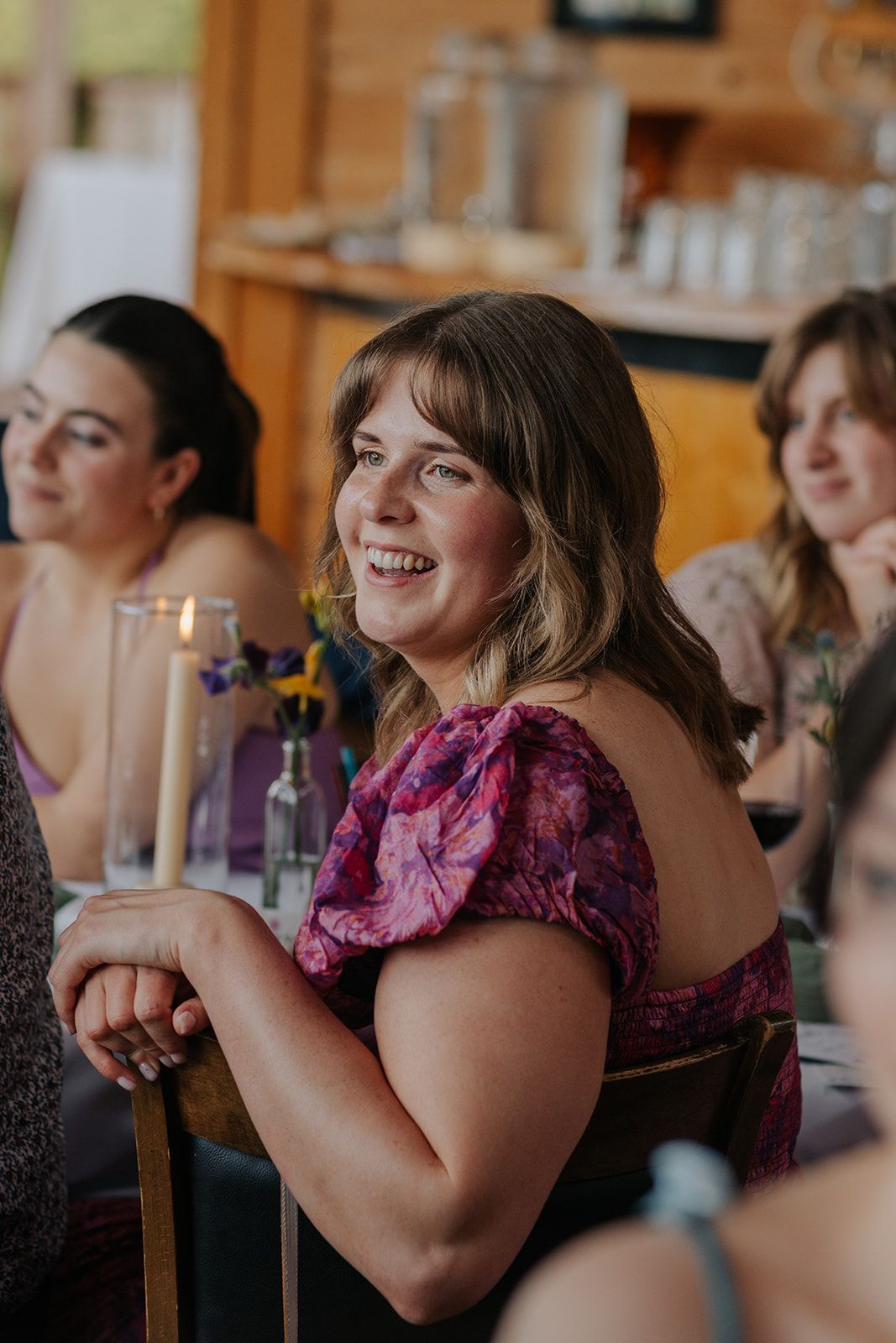 Wedding guest in pink floral dress smiles warmly during reception celebration.