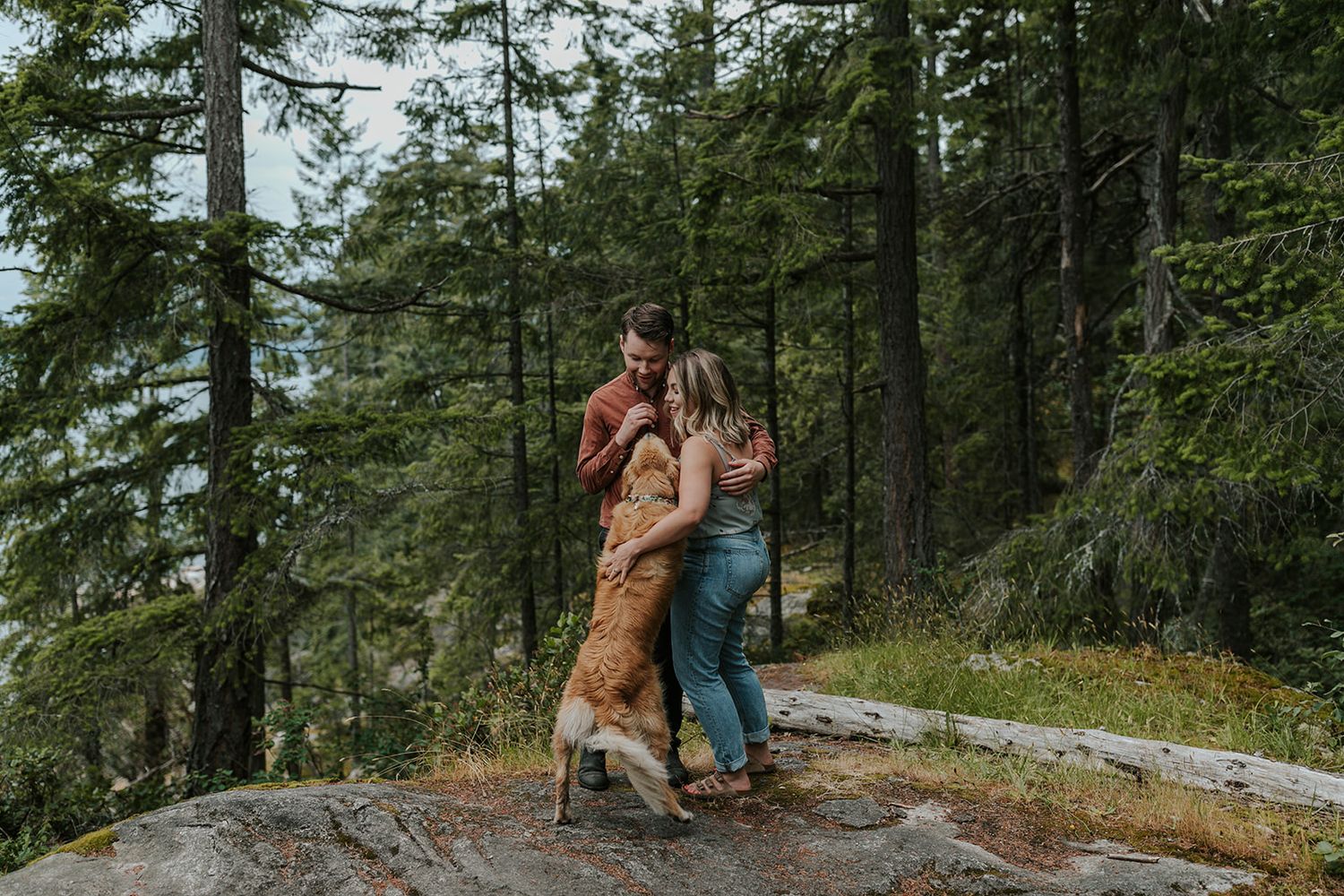 A couple walks through a scenic forest path with their dog.