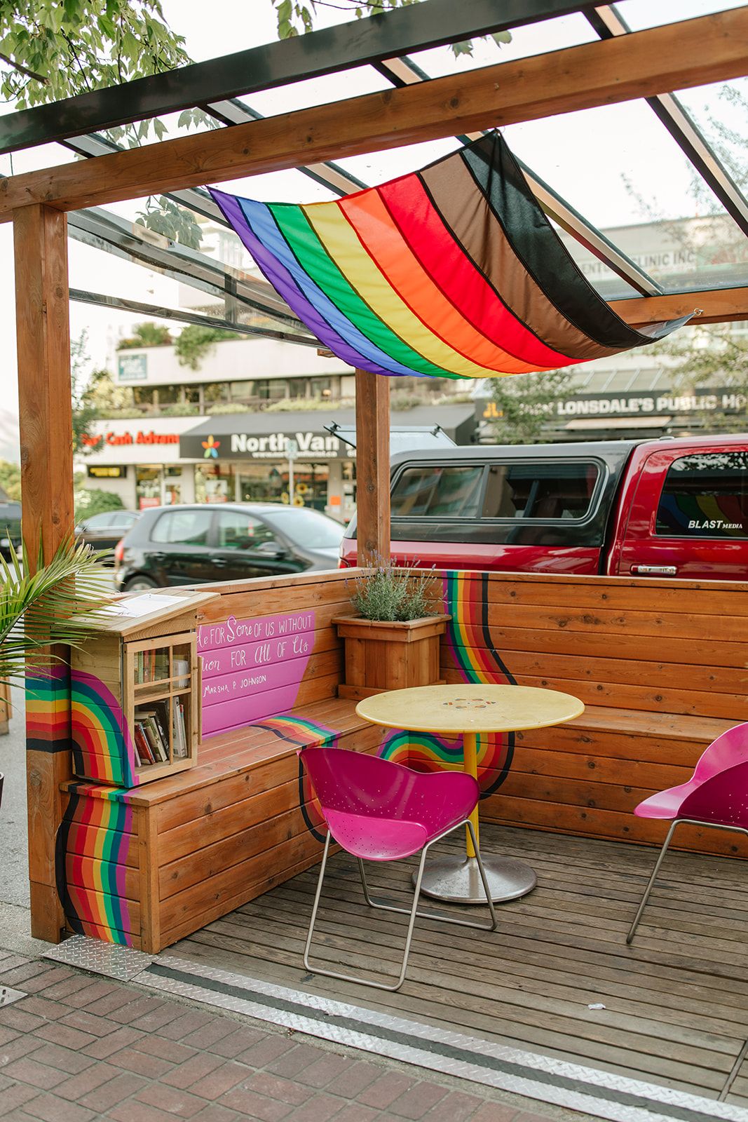 Outdoor patio seating area with rainbow pride flag decor and wooden benches.