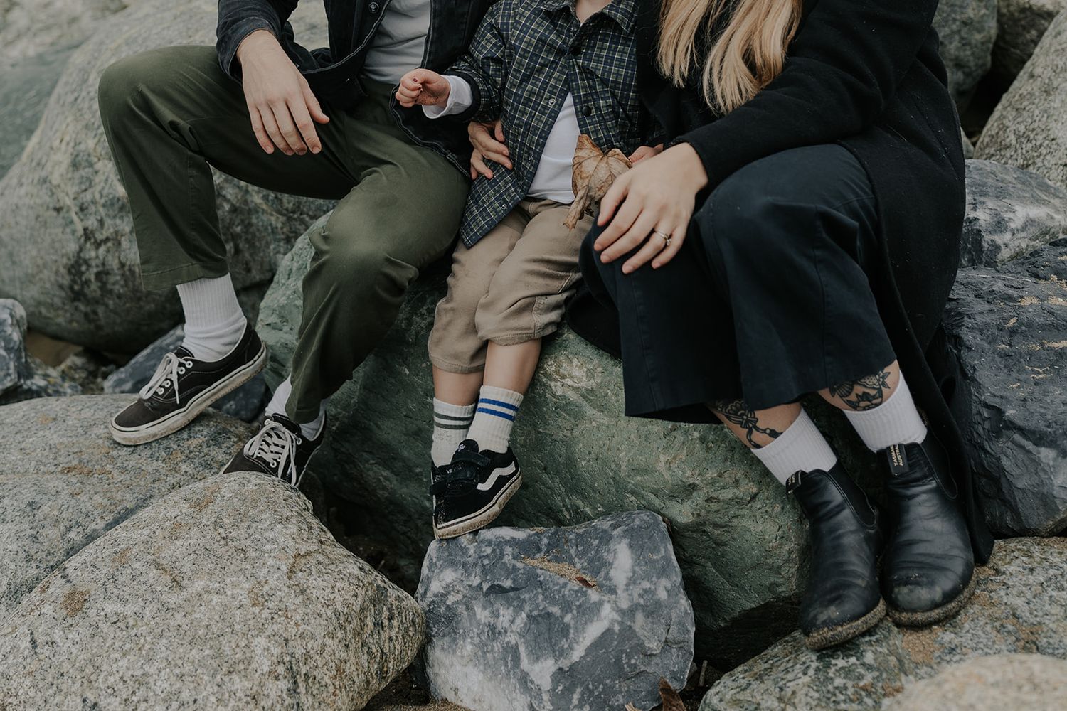 Family members sitting together on rocky coastal outcrop.