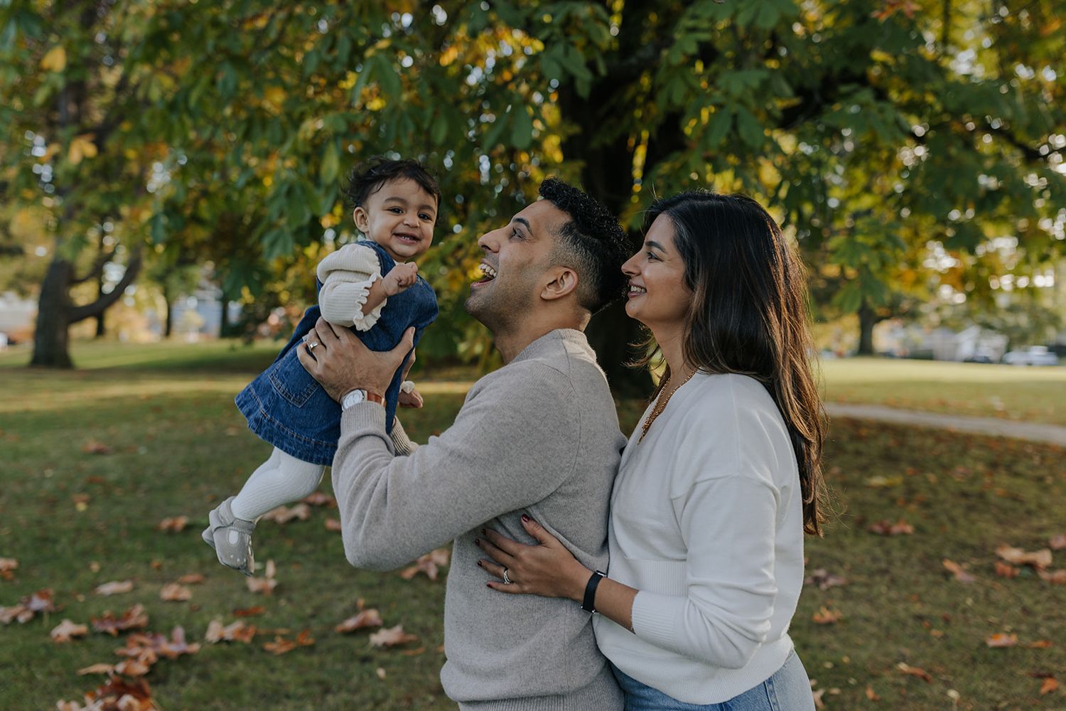 A joyful family photoshoot outdoors with autumn foliage in the background.