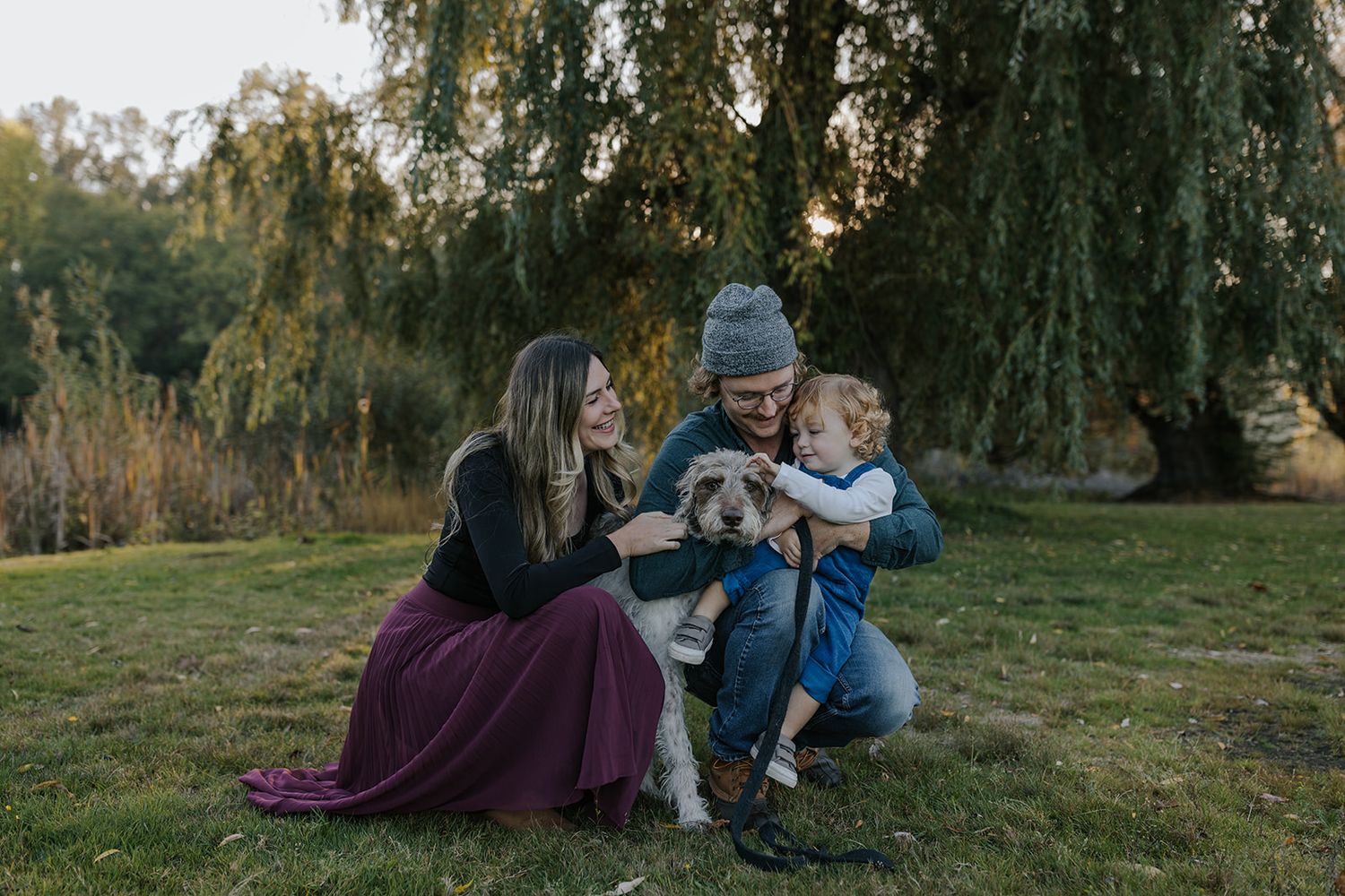 Family relaxing together under willow trees in a serene outdoor setting.