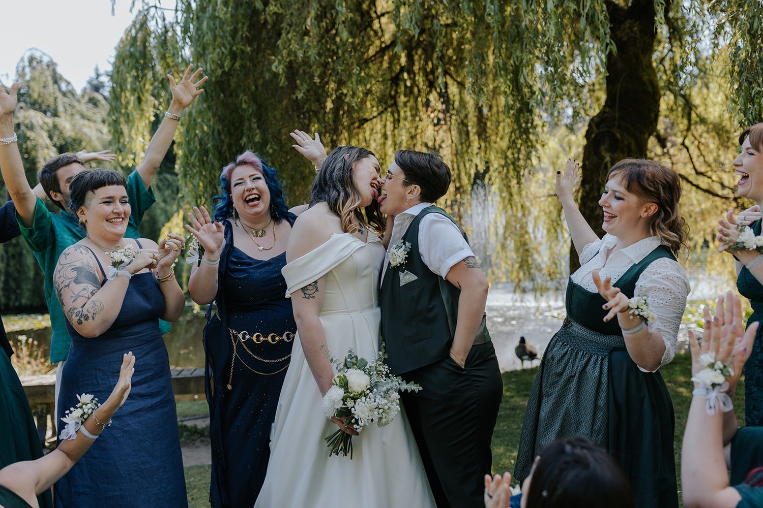 Wedding party celebrates outdoors under weeping willow trees.
