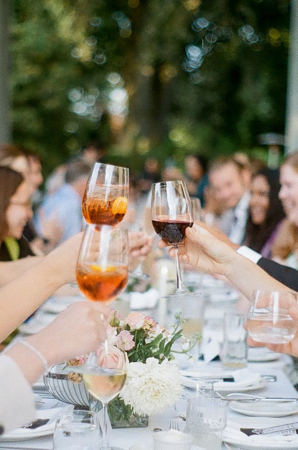 Wedding reception table with raised wine glasses and floral centerpieces in outdoor setting.