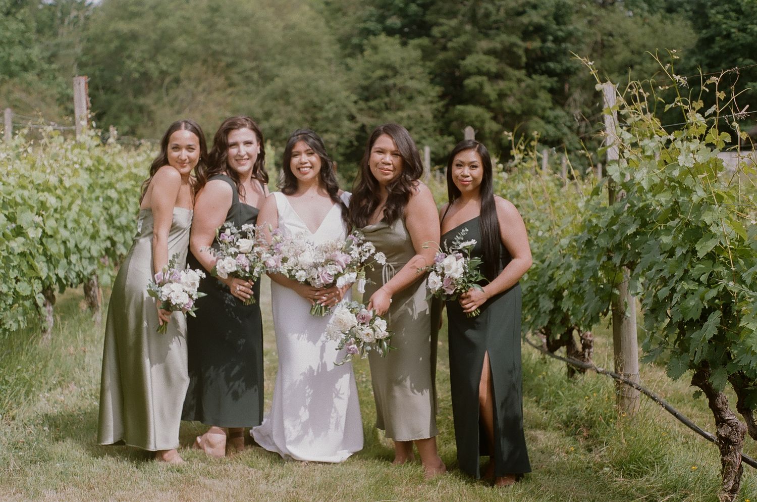 Wedding party posing together in a scenic vineyard setting.