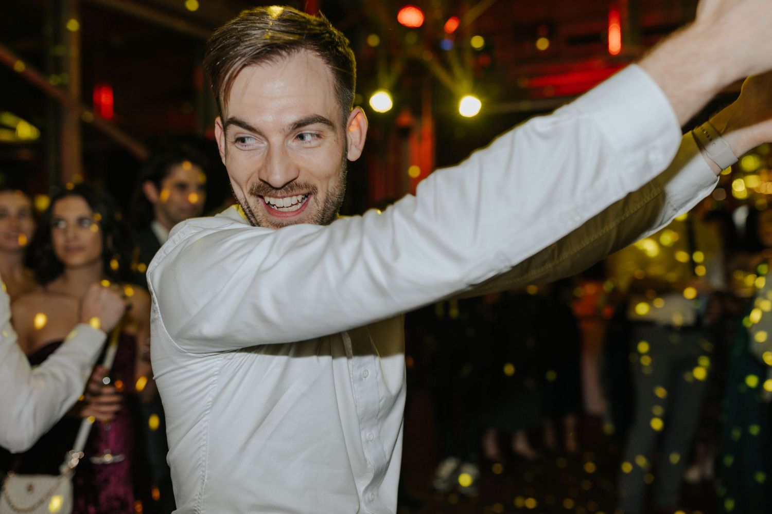 Wedding guests dance joyfully under colorful party lights at a reception celebration.