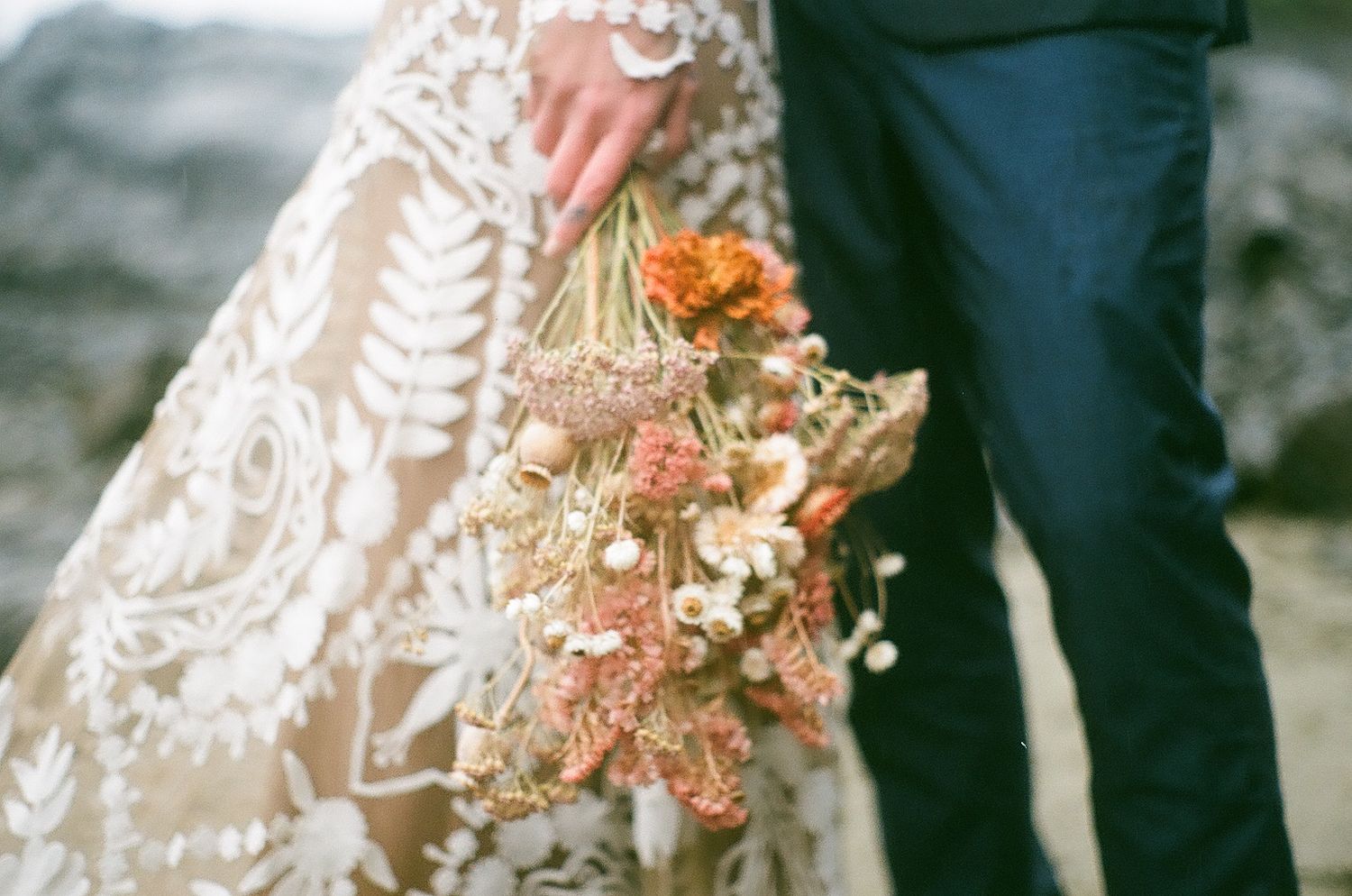 A wedding bouquet with dried flowers and peach blooms hangs beside a lace dress.