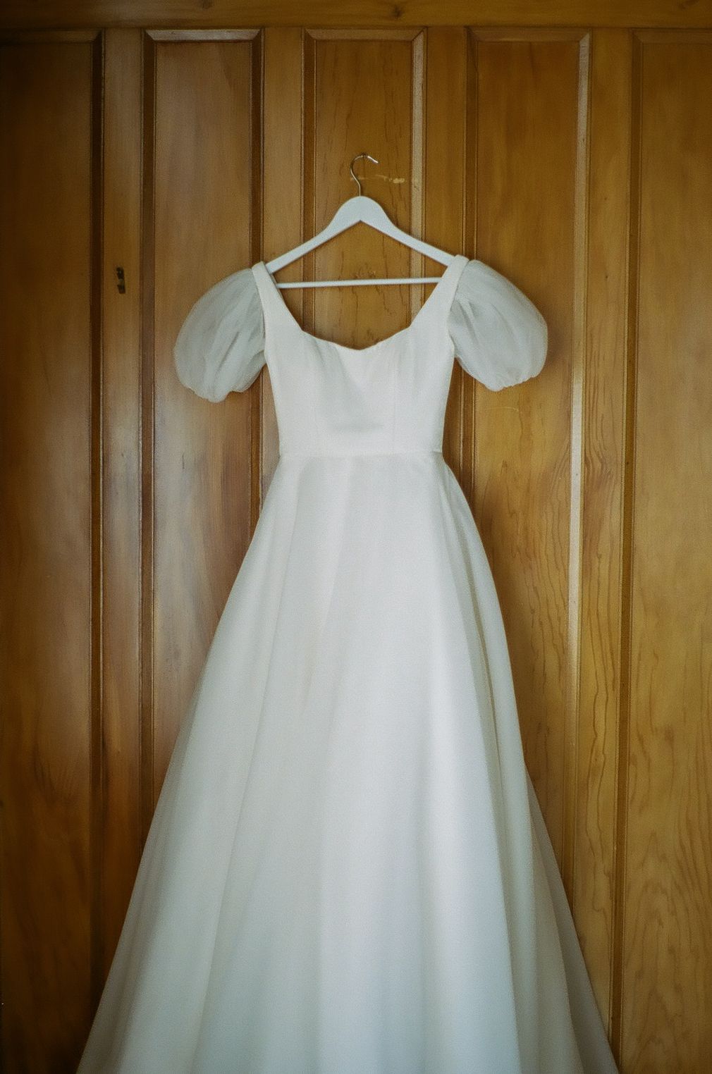 White wedding dress hanging on wooden wall panels.