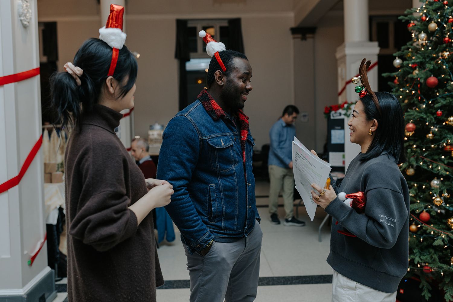 People gathered in indoor space decorated with Christmas trees and holiday decorations.