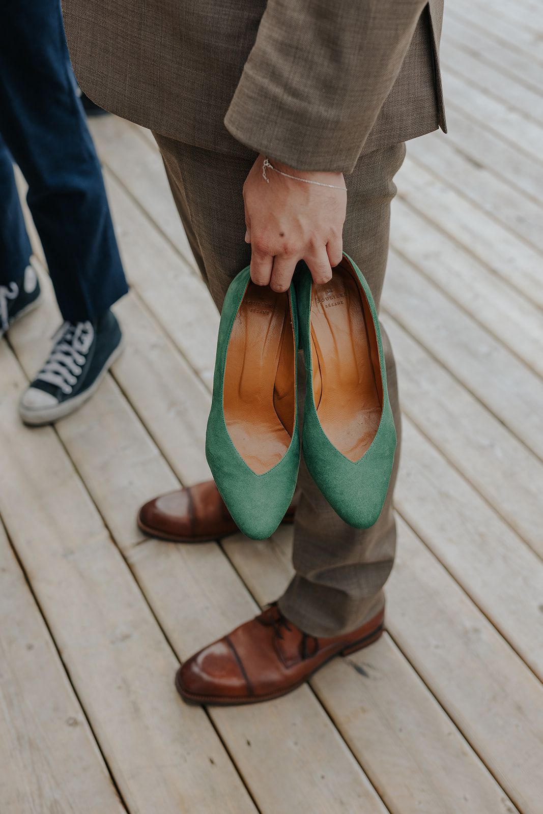 Close-up of brown leather and mint green shoes on wooden deck.