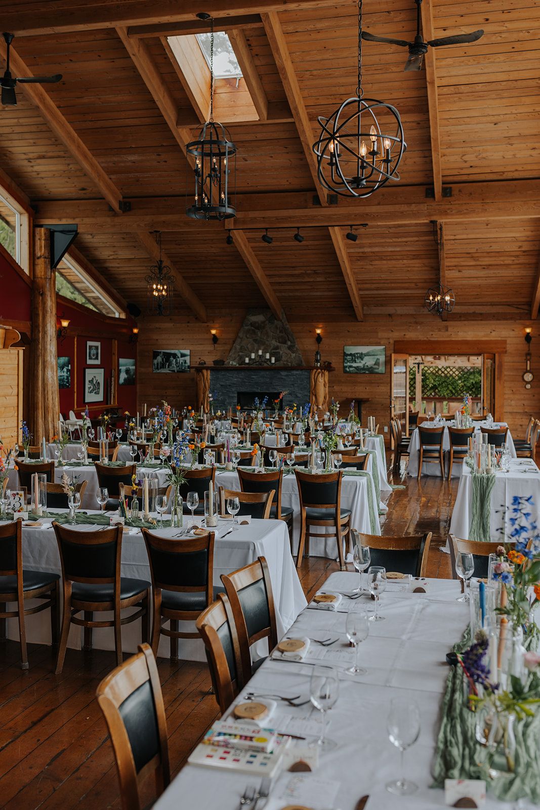 Rustic wooden reception hall with vaulted ceiling, chandeliers and tables set for a wedding celebration.