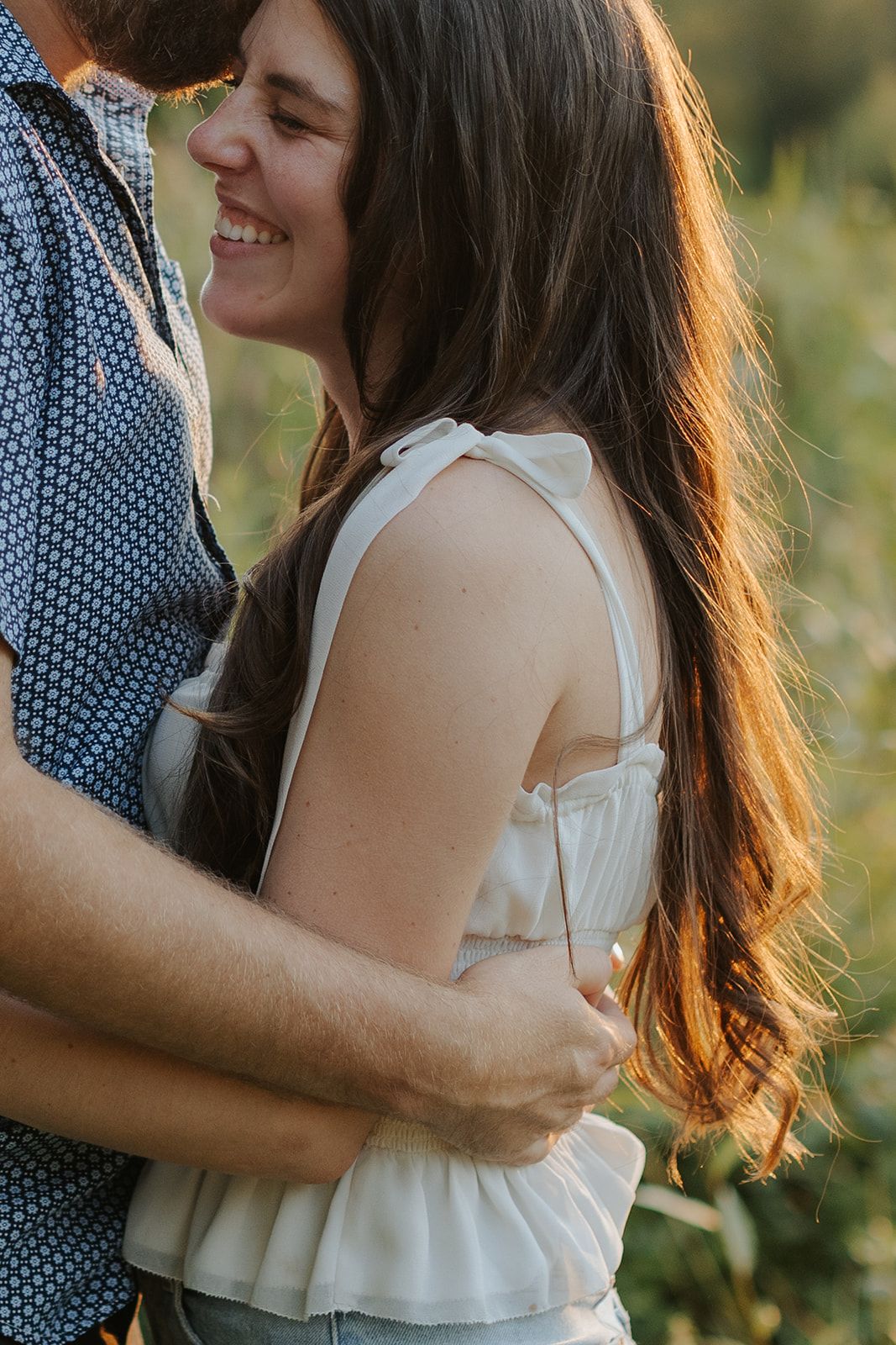 A romantic couple embraces in warm sunlight during an intimate outdoor photoshoot.