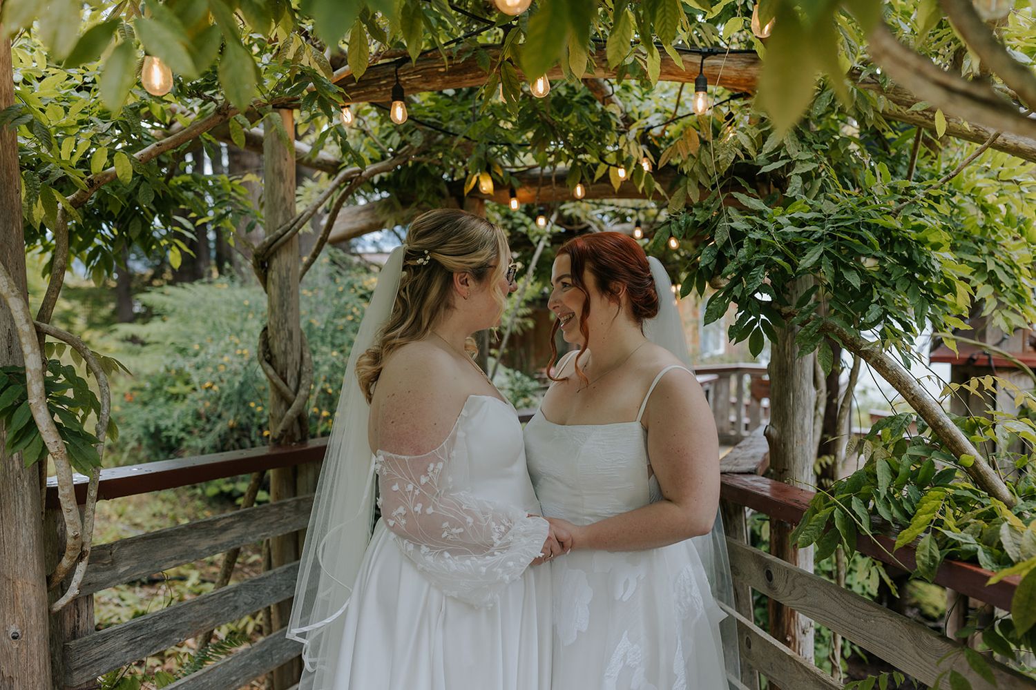 Two people in white wedding dresses share an intimate moment under blooming trees.