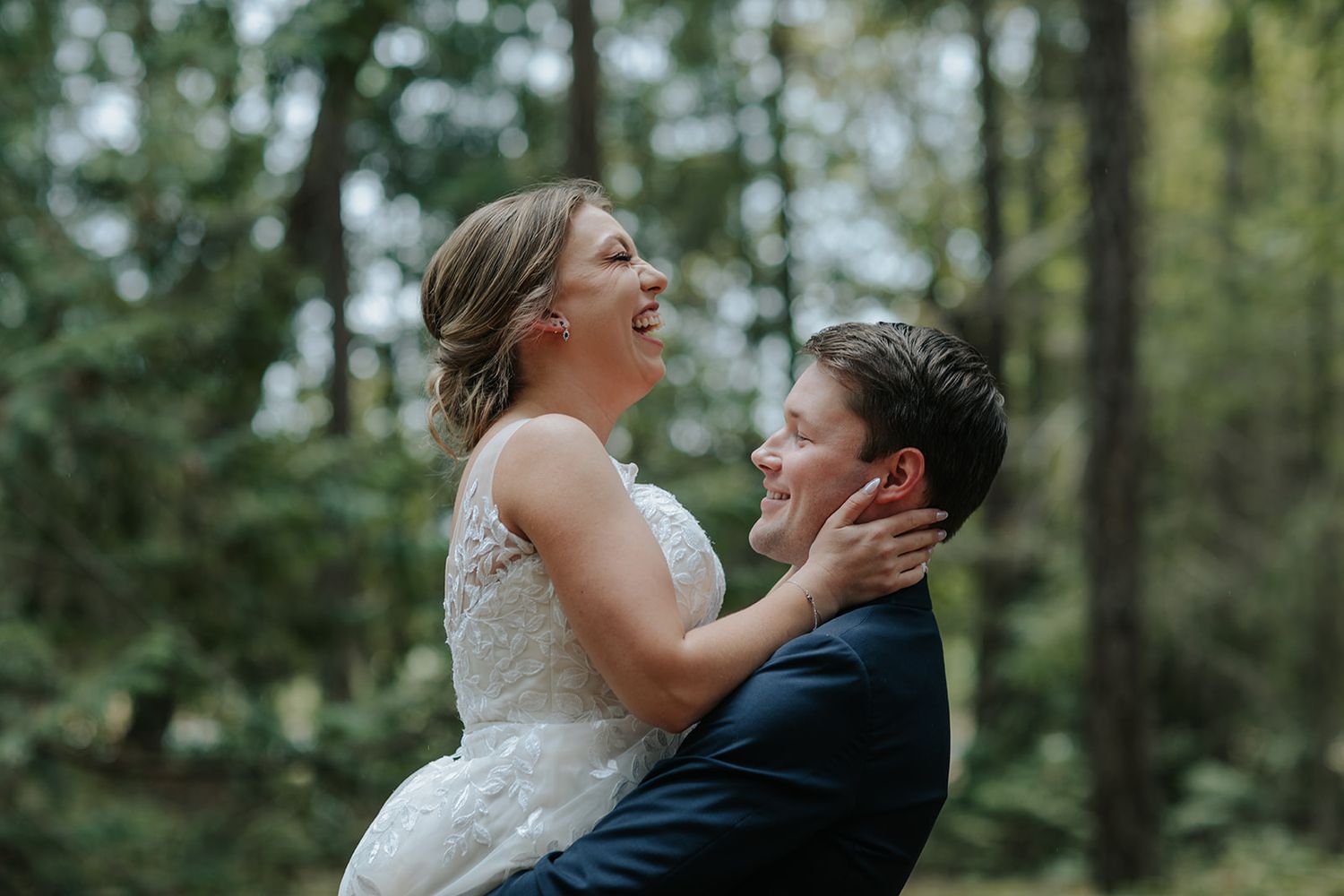 A joyful couple shares a candid laughing moment in a forest setting.