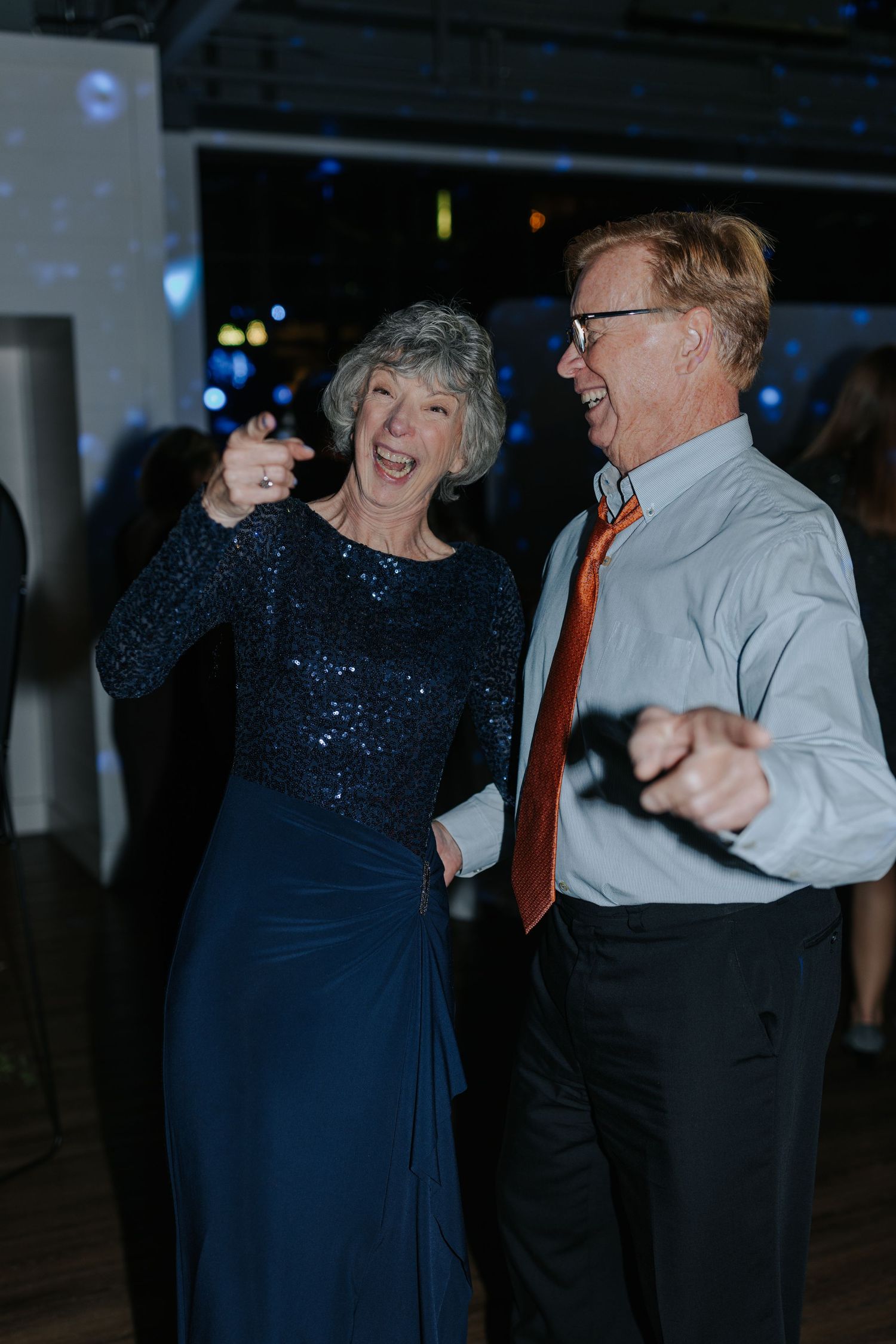 Wedding guests dance joyfully on the dance floor, with the woman wearing a sparkly navy dress.