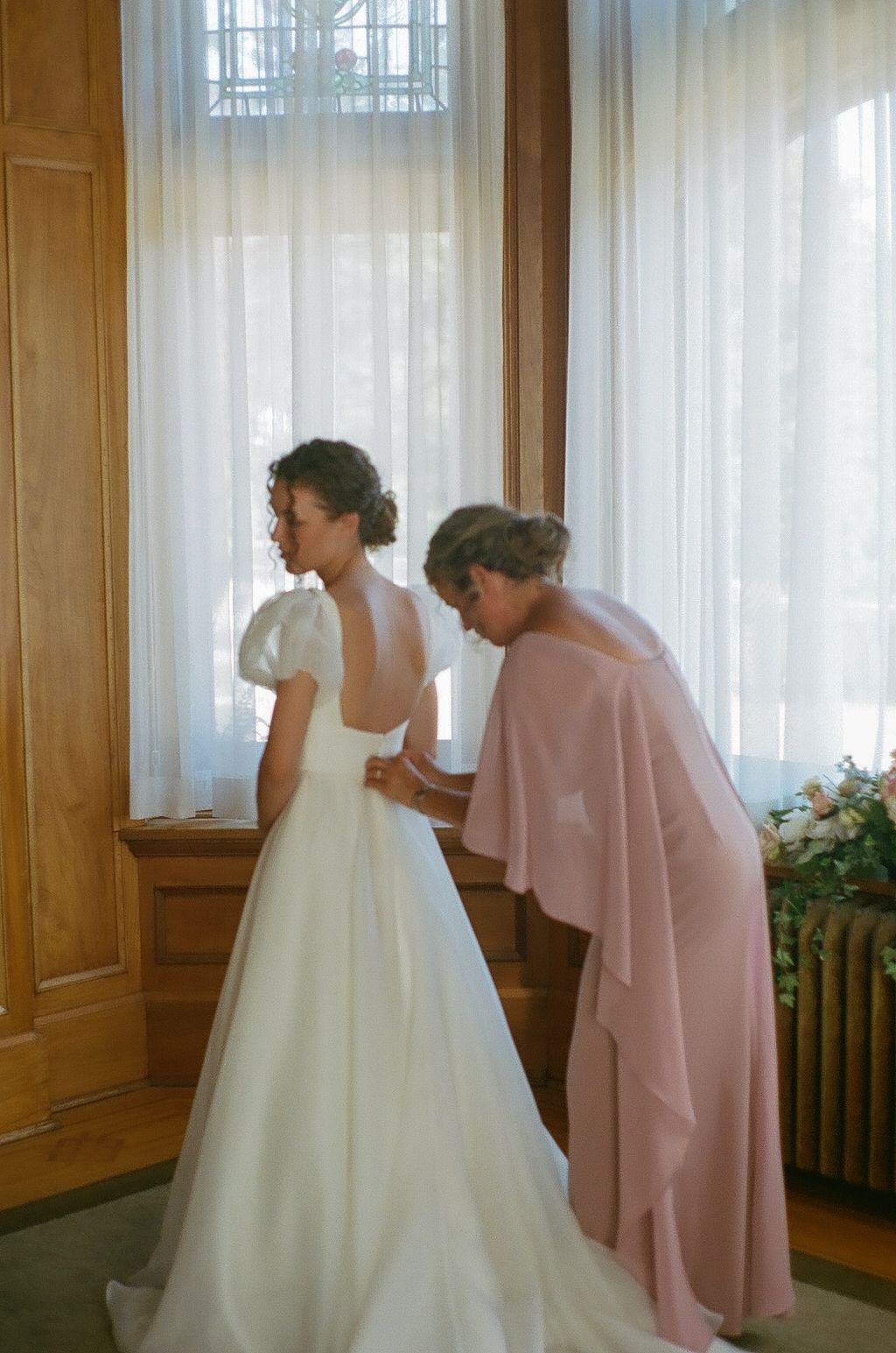 Wedding dress being adjusted in sunlit room with wooden panels.