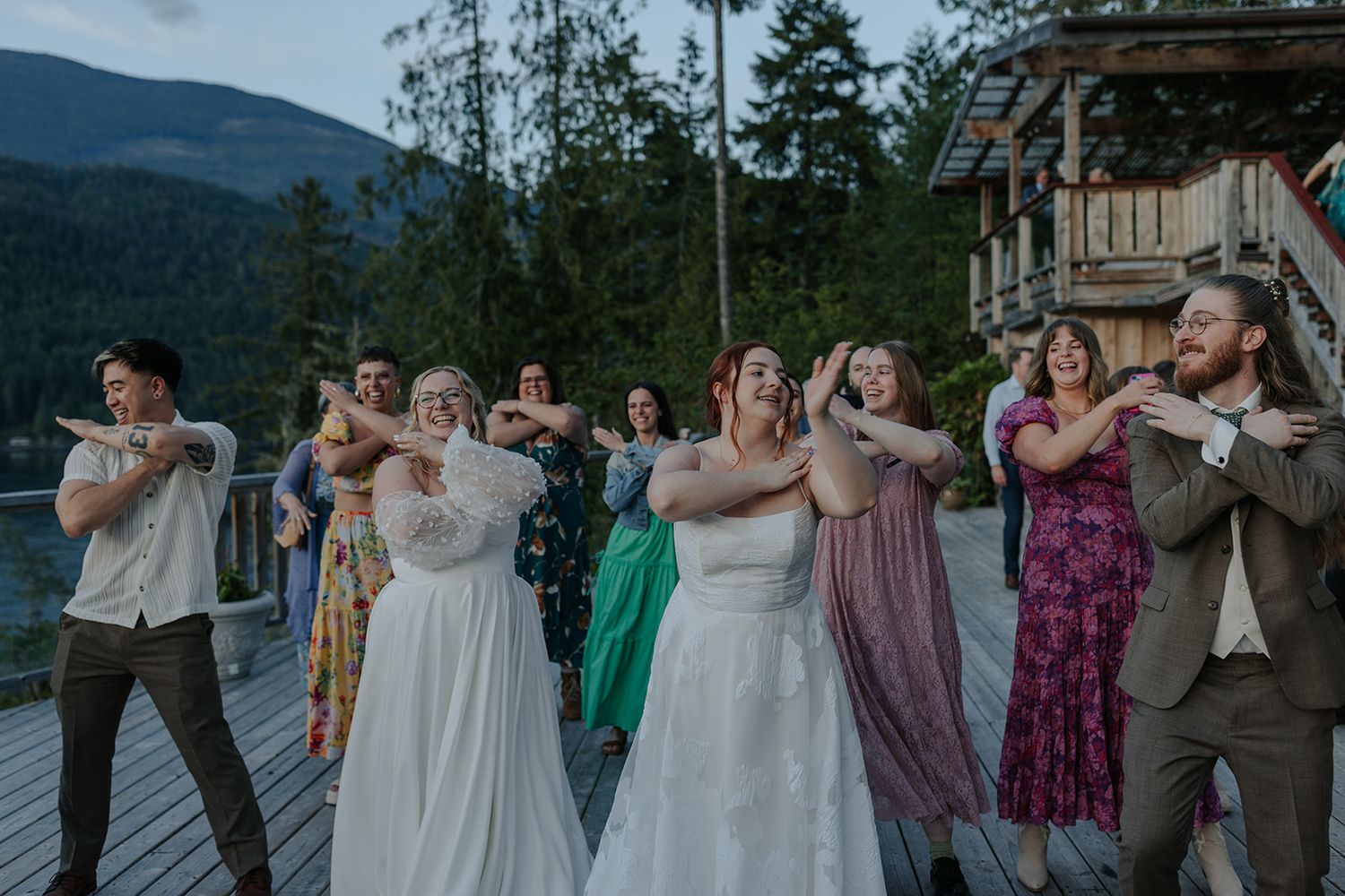 Wedding party celebrates outdoors with mountains and trees creating a scenic backdrop.
