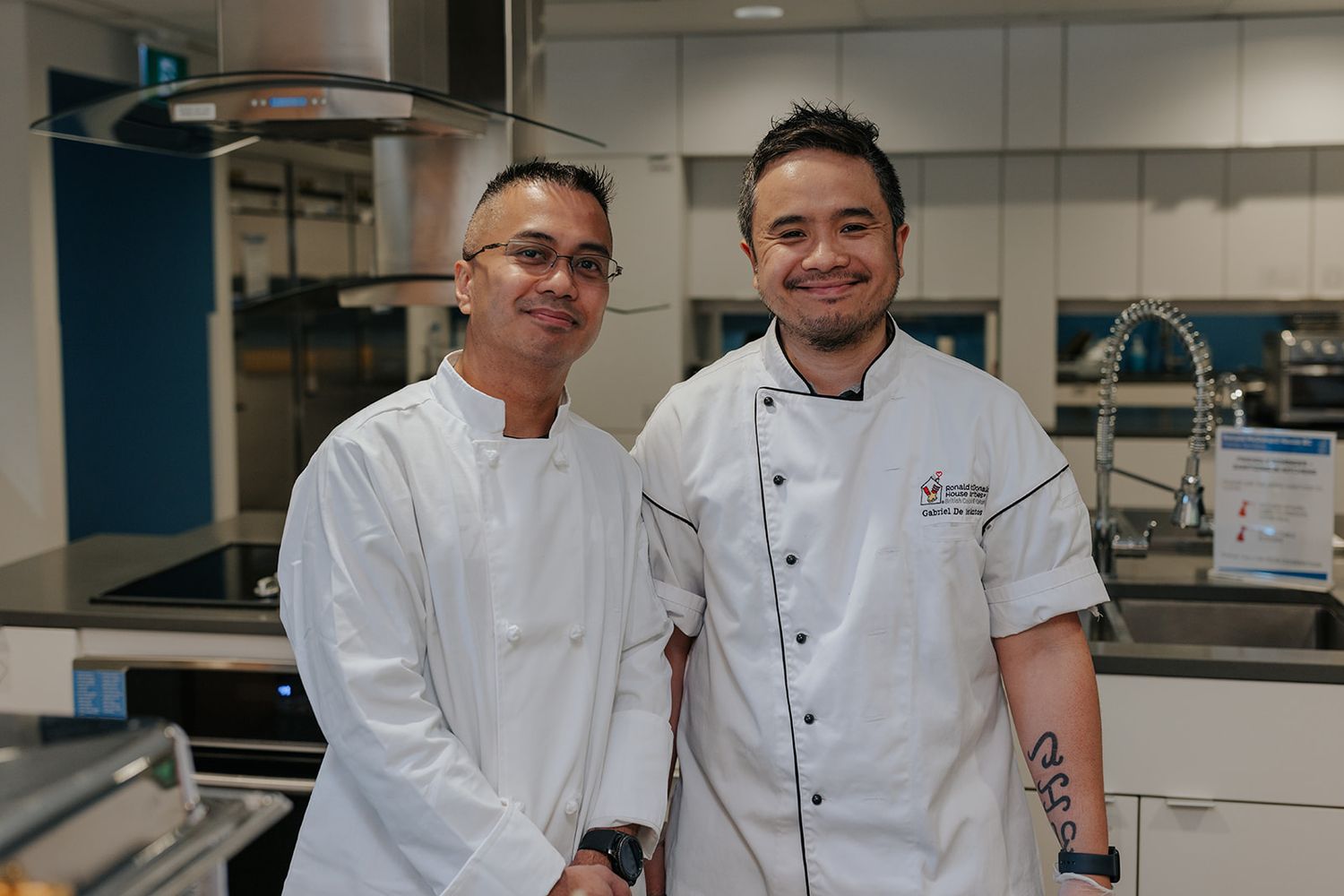 Professional chefs in white uniforms standing together in a commercial kitchen.
