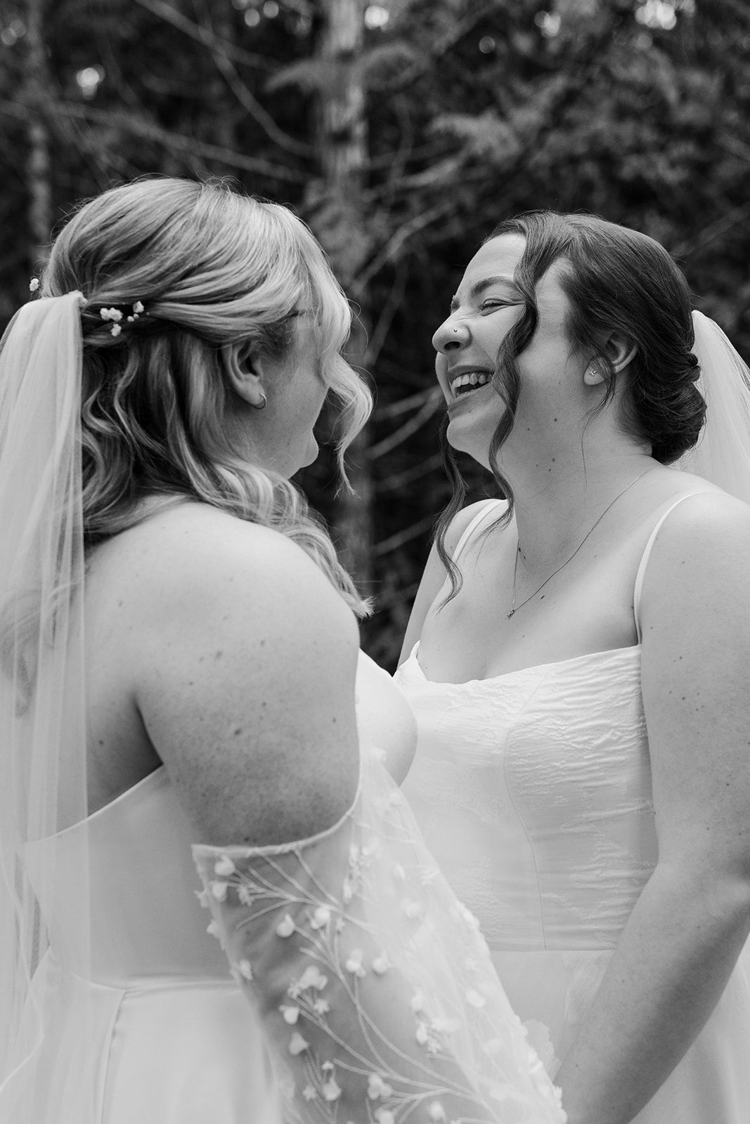 Black and white close-up of two brides laughing together during their wedding photoshoot.