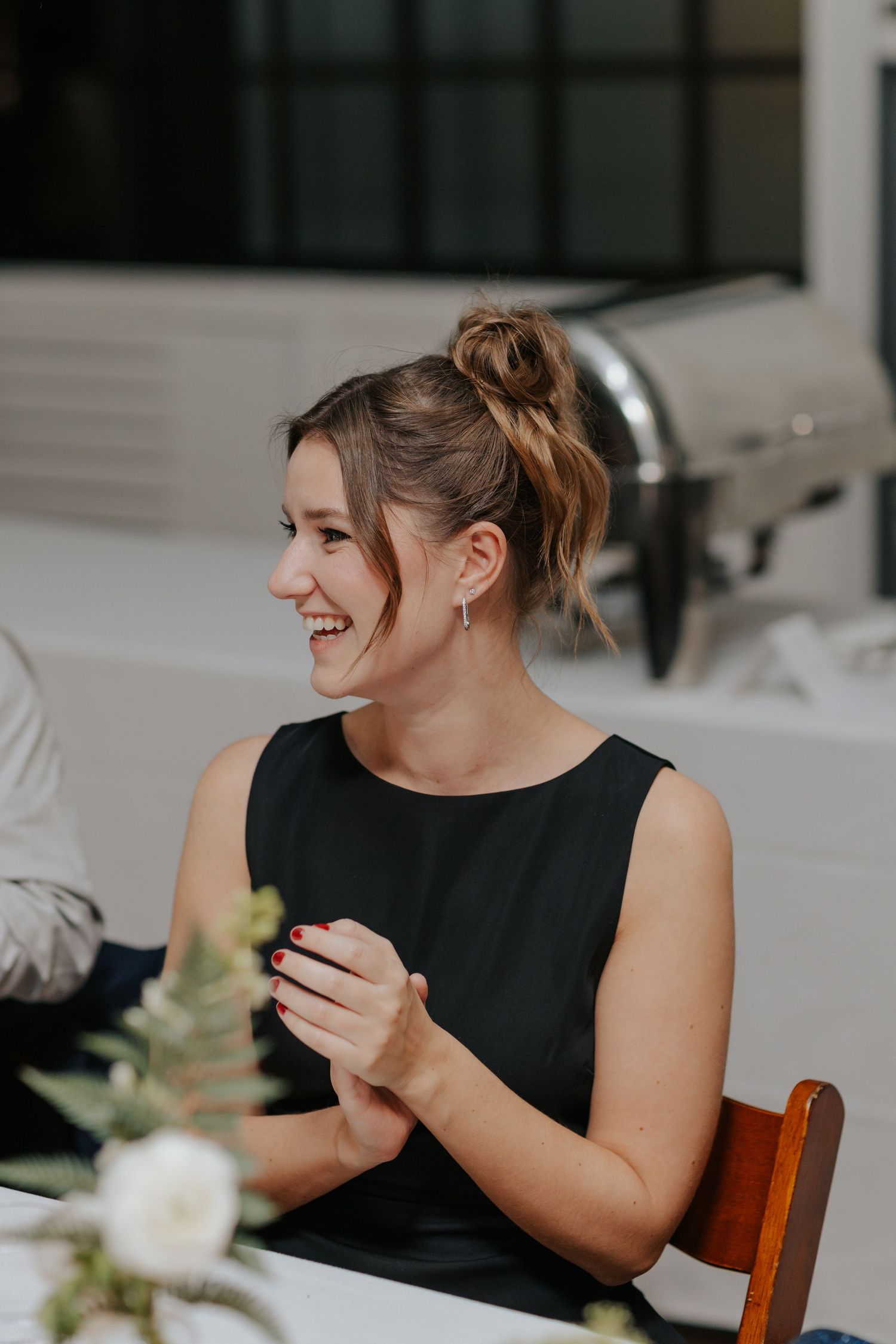 A guest in a black sleeveless dress laughs during a wedding reception.