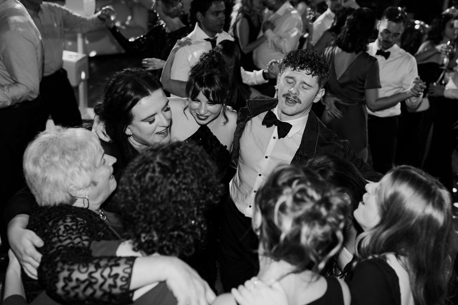 A crowded dance floor filled with celebrating wedding guests in formal attire.