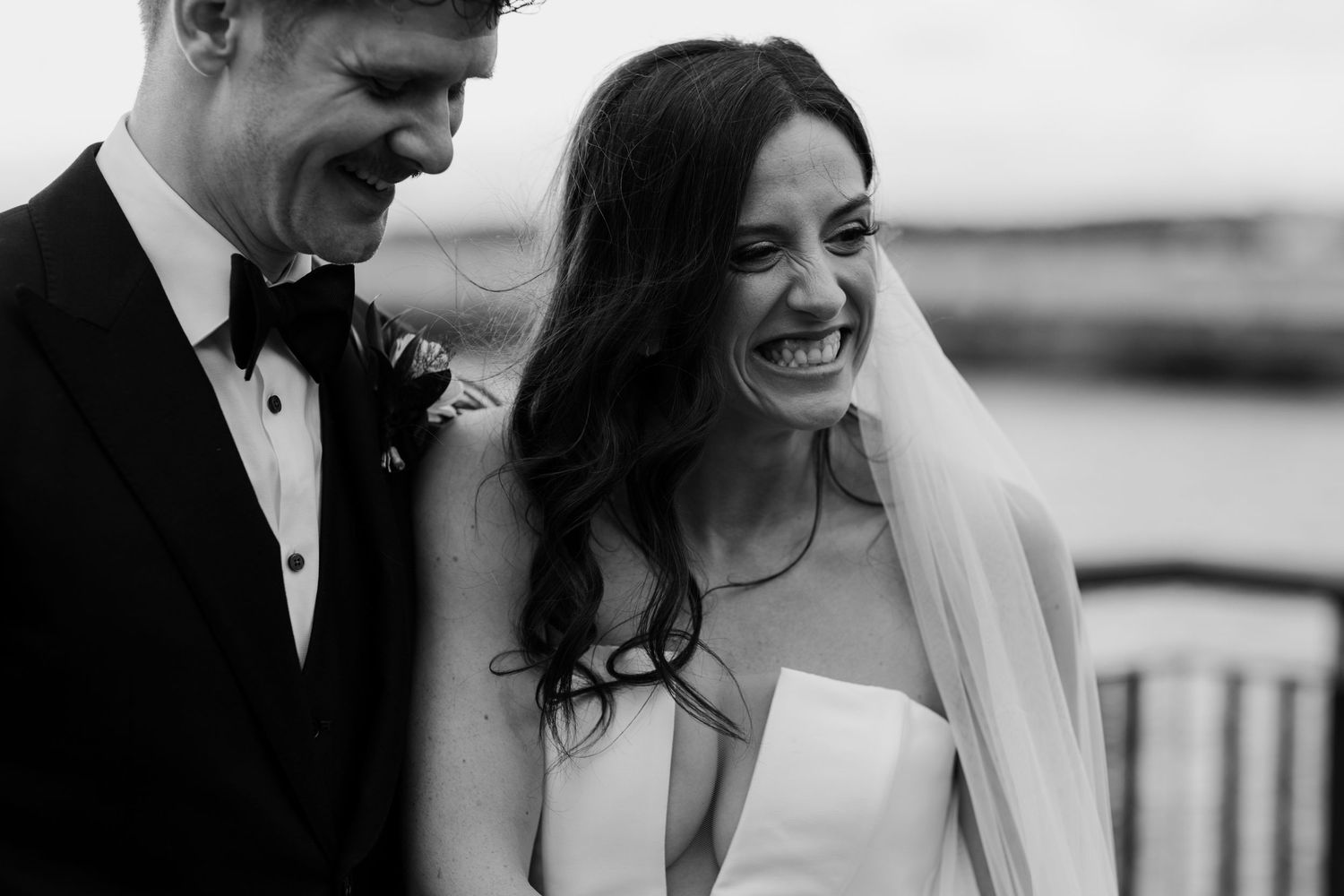 A wedding couple shares a candid moment of laughter during their black and white portrait session.