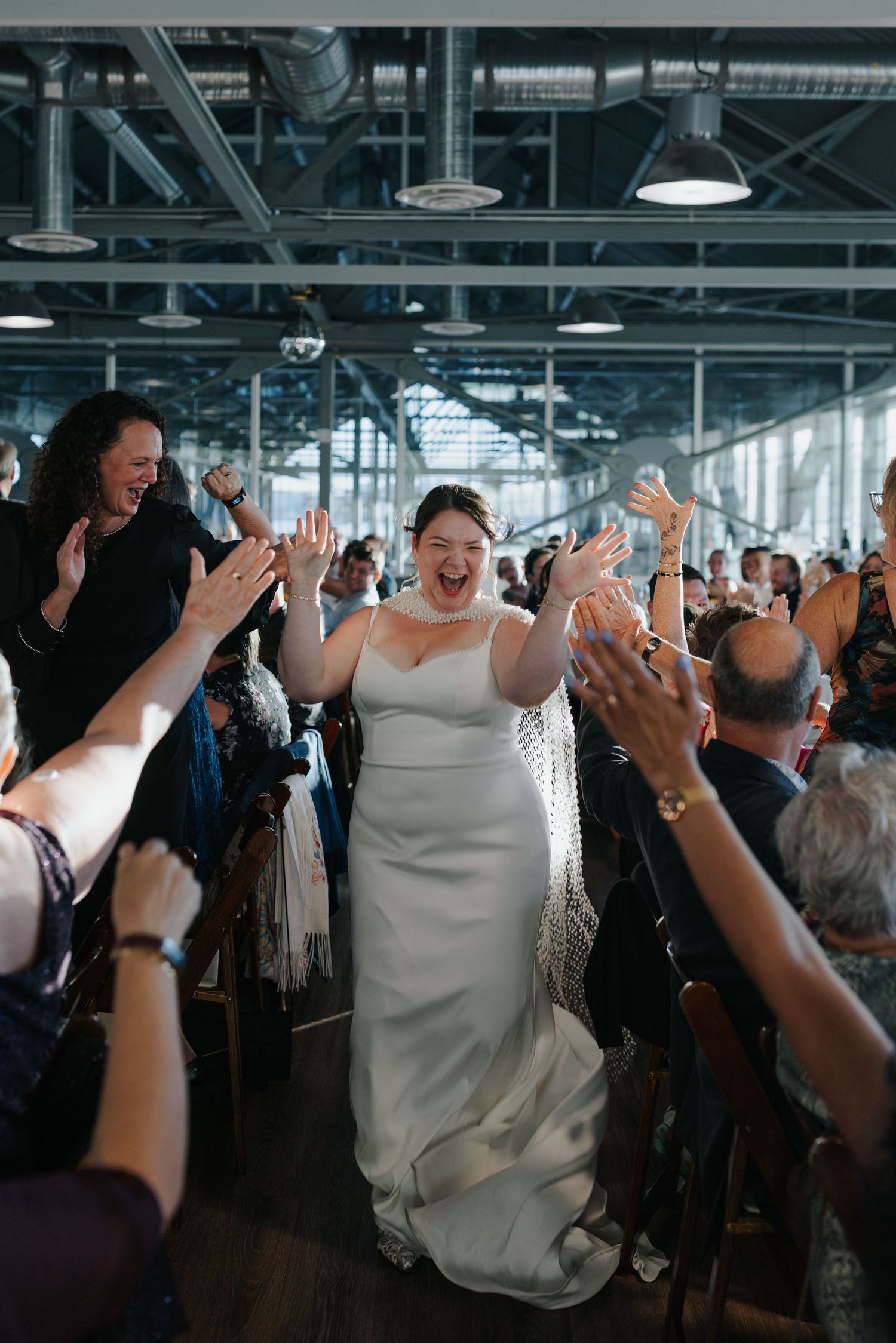 Wedding celebration with guests raising hands in joy at an industrial-style indoor venue.