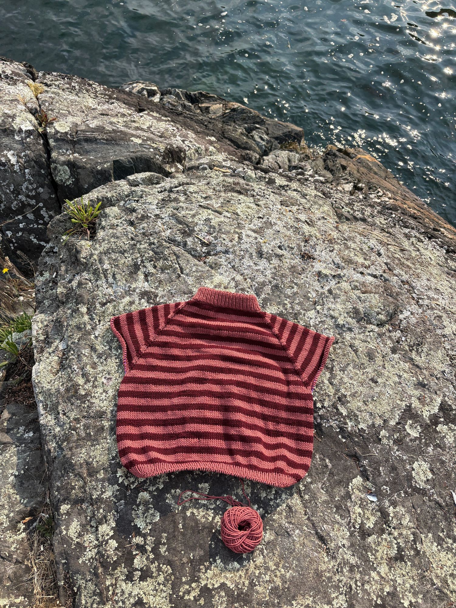 A red and black striped knit scarf laid out on a rocky surface near water.