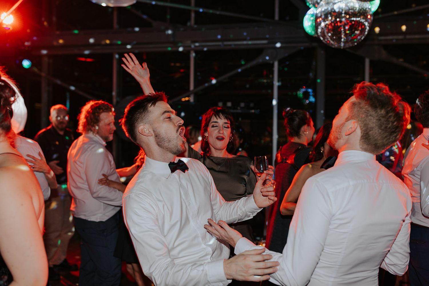 Energetic dance floor celebration with guests in formal attire under red lighting.