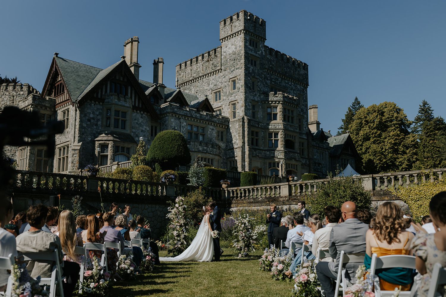 A grand stone castle wedding venue with guests gathered on the manicured lawn.