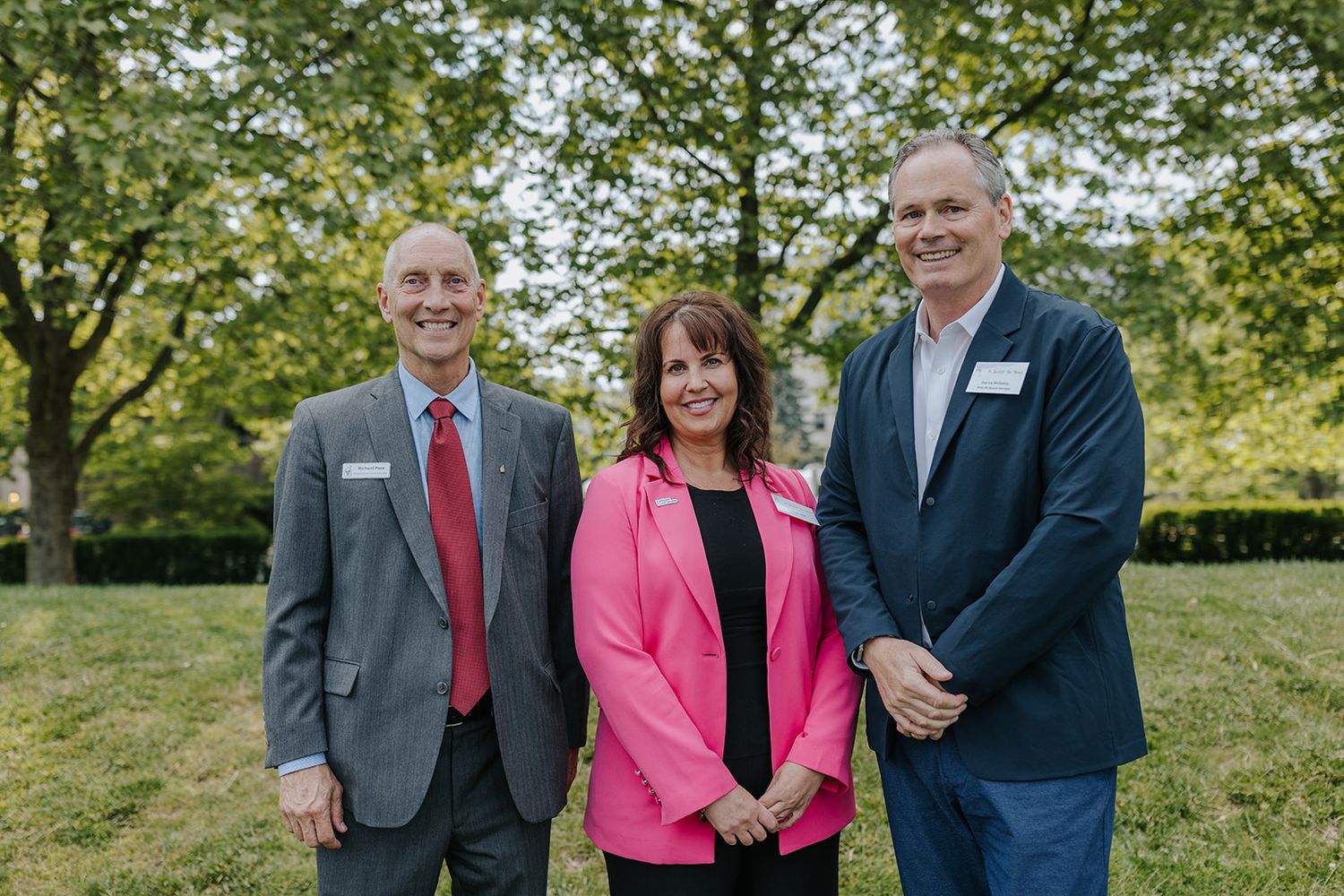 Professional group photo outdoors with people in business attire against green foliage.
