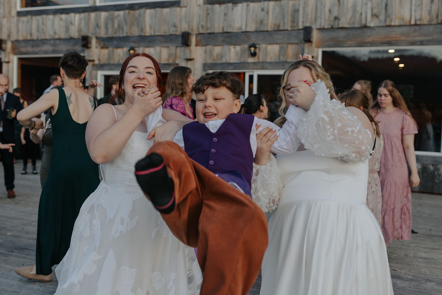 Wedding celebration with dancers in formal attire enjoying themselves on a rustic wooden deck.
