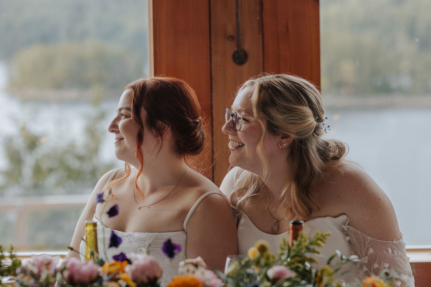 Wedding guests enjoying a meal at tables with scenic lake views through large windows.
